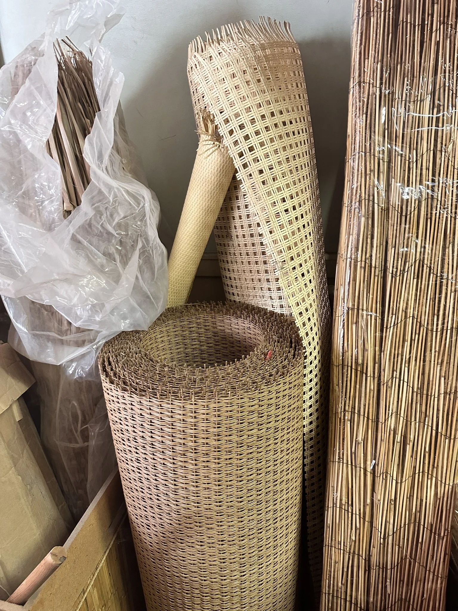 Stacked bamboo and wicker rolls with plastic wrapping on the left and a bamboo roll on the right.