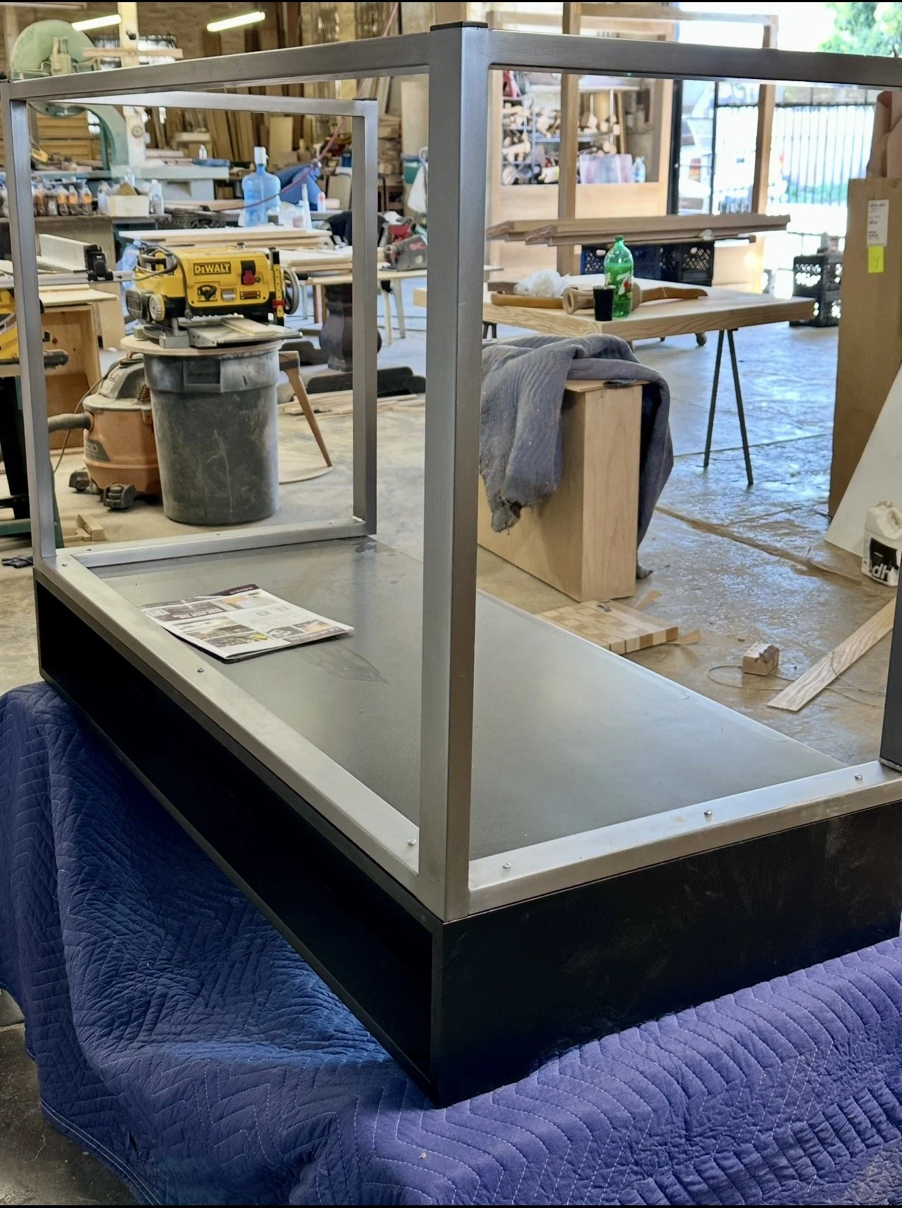 Empty glass display case on a quilted blue blanket in a woodworking workshop.