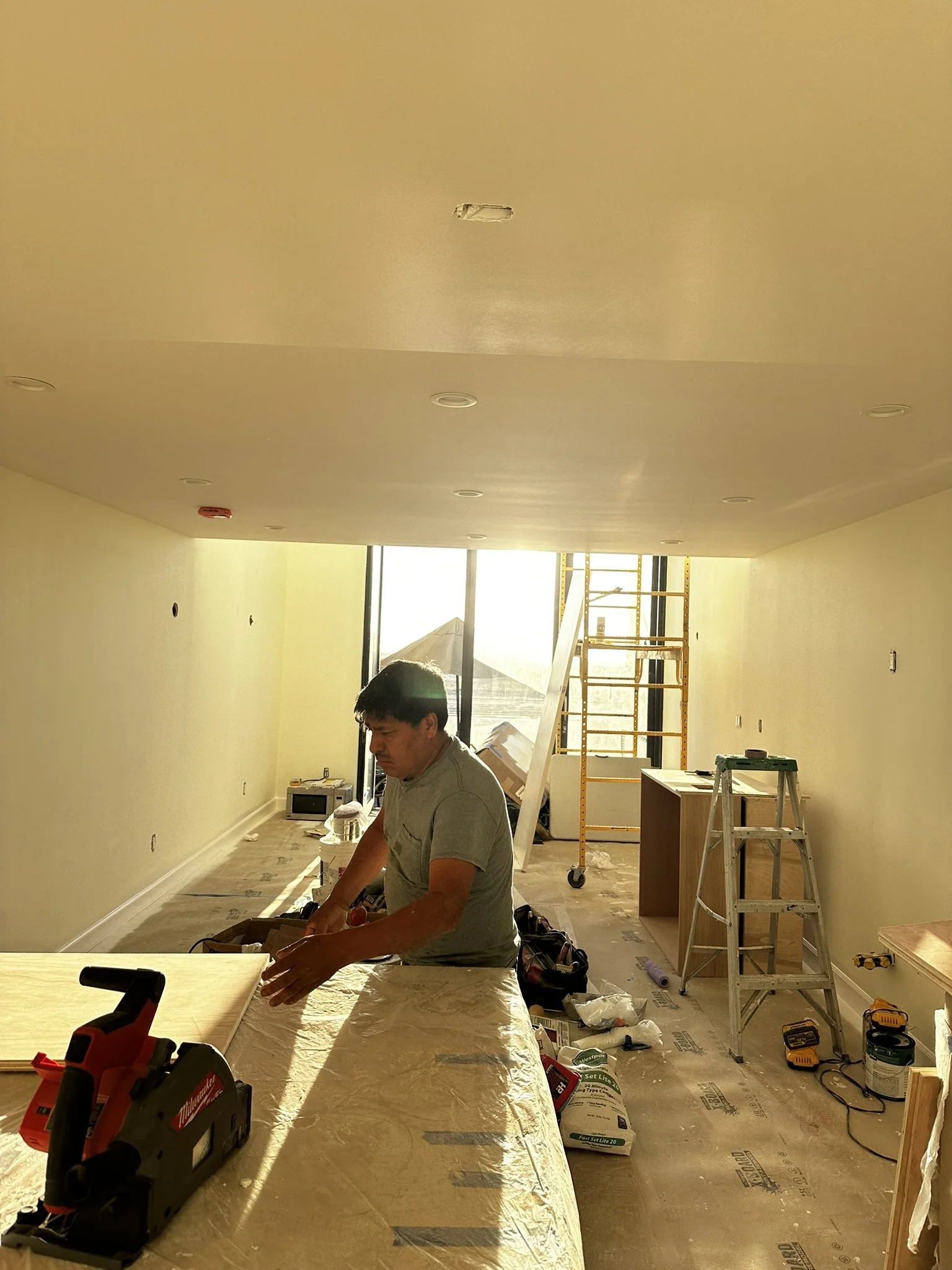 Construction worker installing drywall in a room with construction tools and scaffolding.