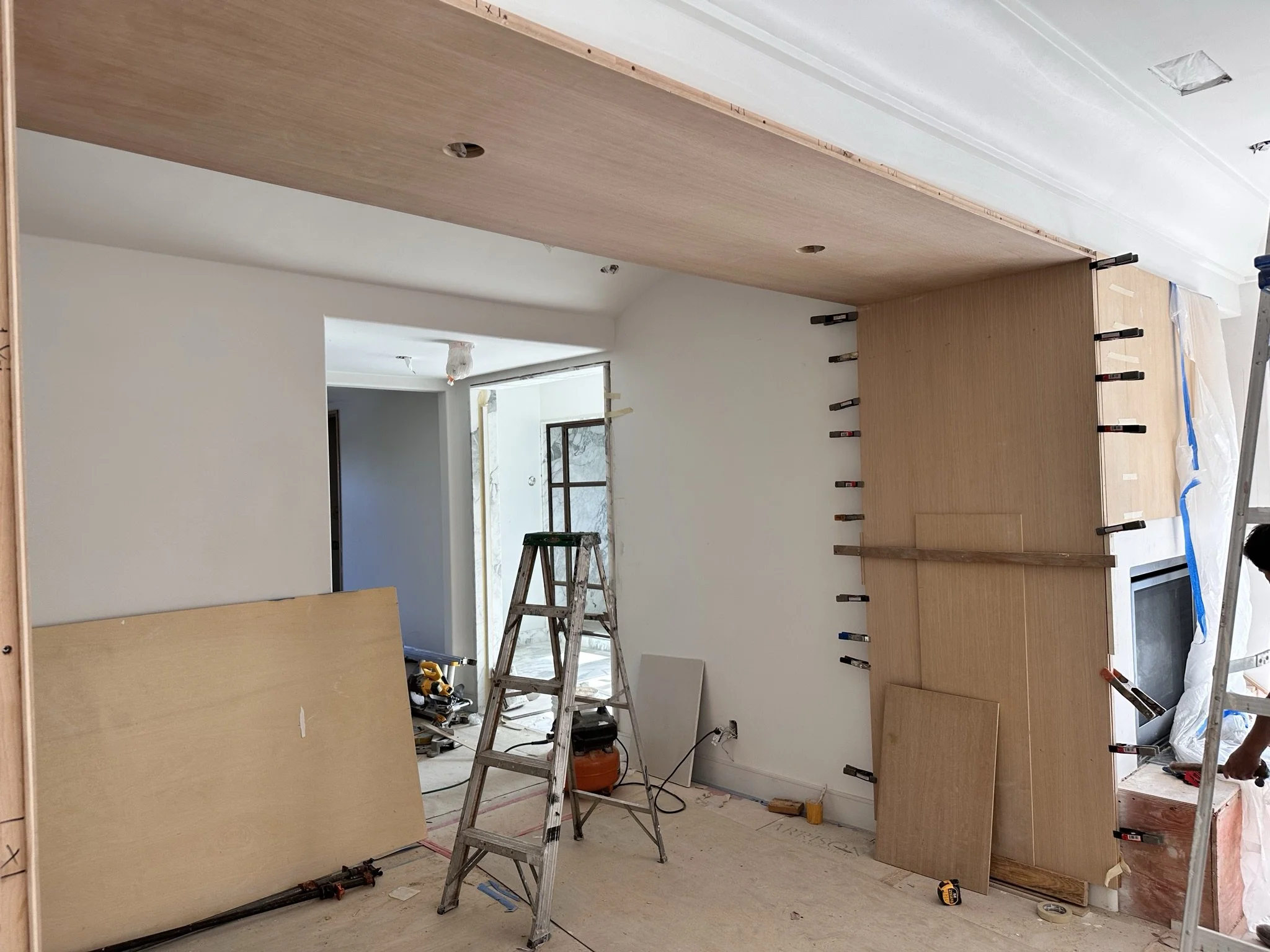Interior of a house under construction, with wooden cabinets being installed and scaffolding and tools visible.