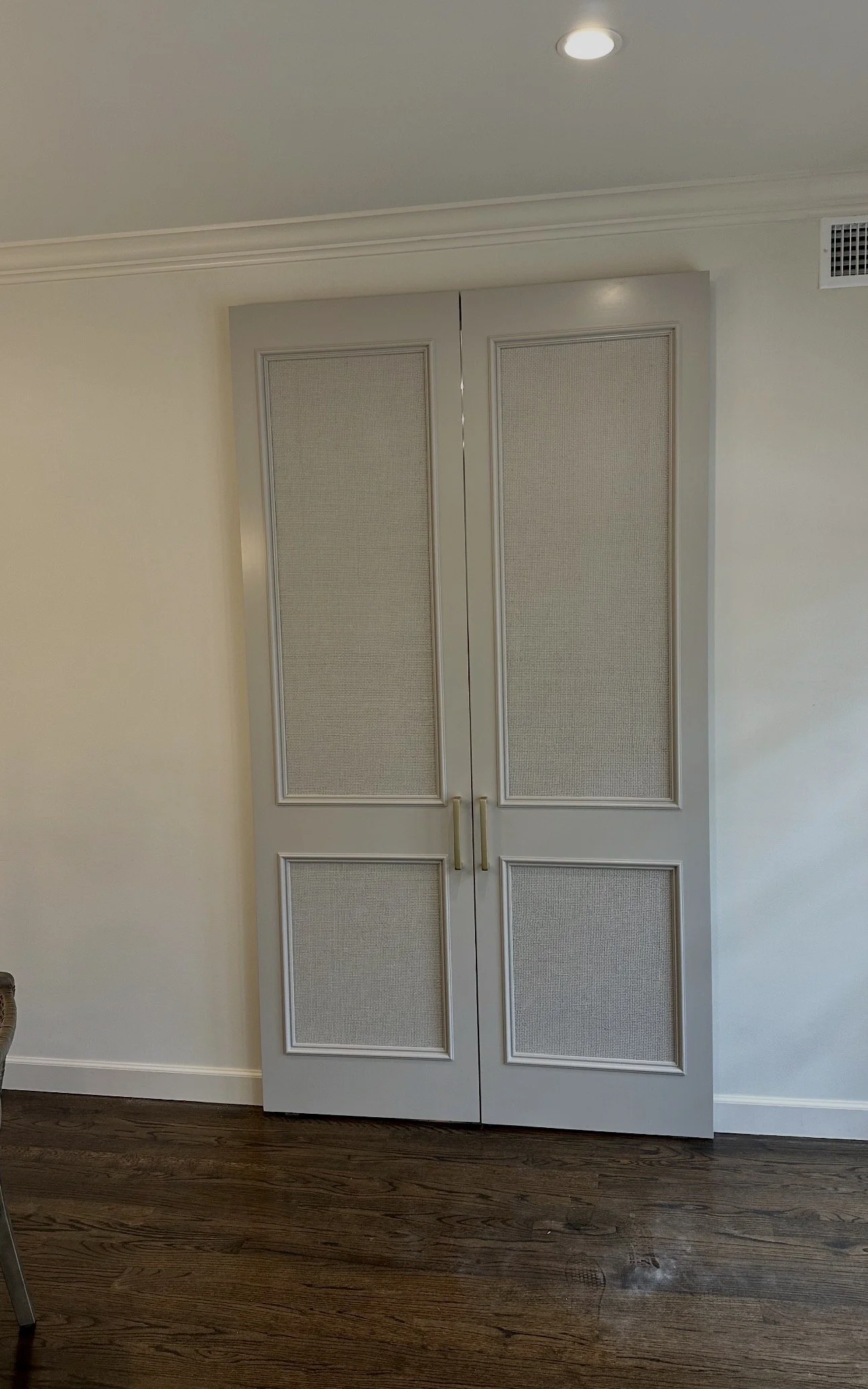 White double closet doors with beige mesh panels and gold handles, set in a beige wall with crown molding and dark hardwood flooring.