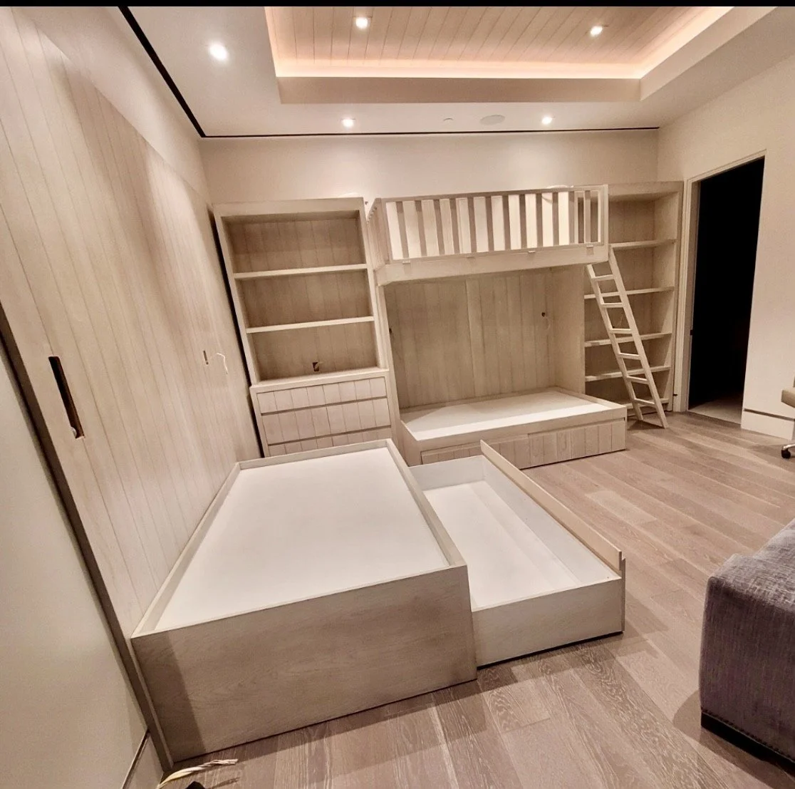 Empty bedroom with a custom-built light wood bunk bed, bookshelves, and storage drawers, with a sliding closet door and hardwood flooring.
