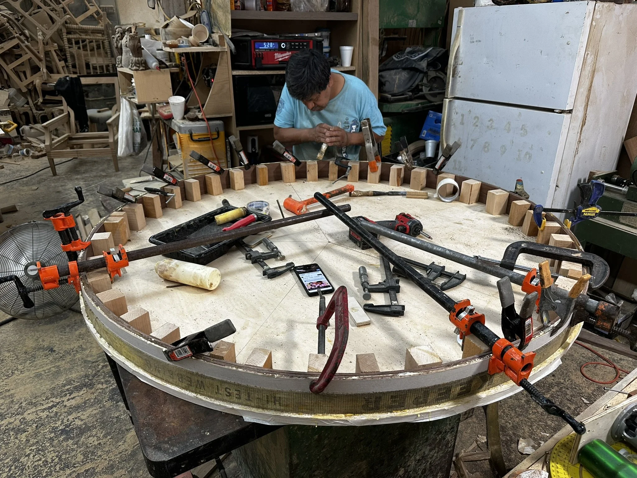 A man working on a wooden boat in his workshop, surrounded by tools and woodworking materials.