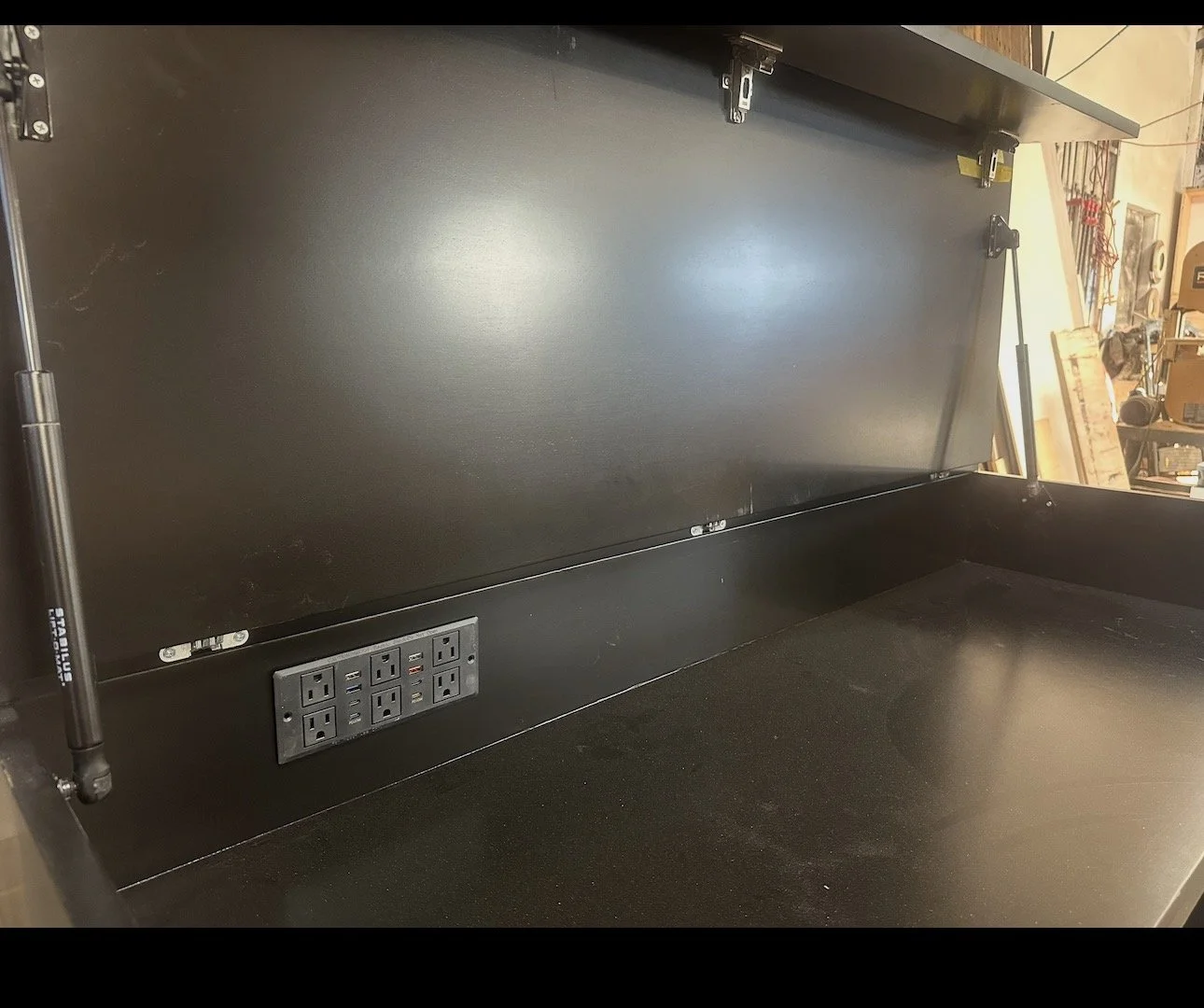 Empty black workbench with a power strip and rack mount power outlets, in a workshop or garage setting.