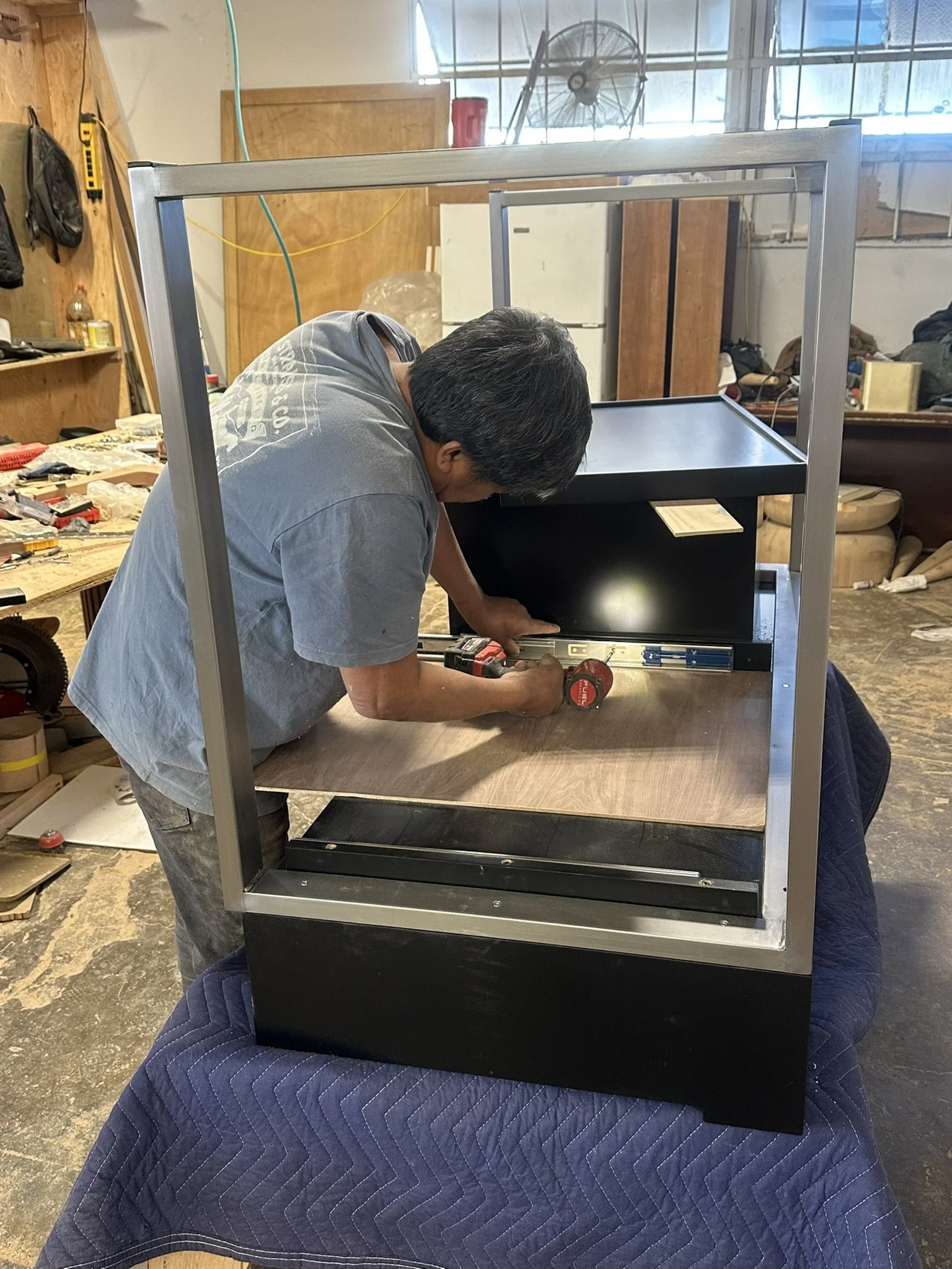 Person working on assembling a black cabinet frame in a workshop.
