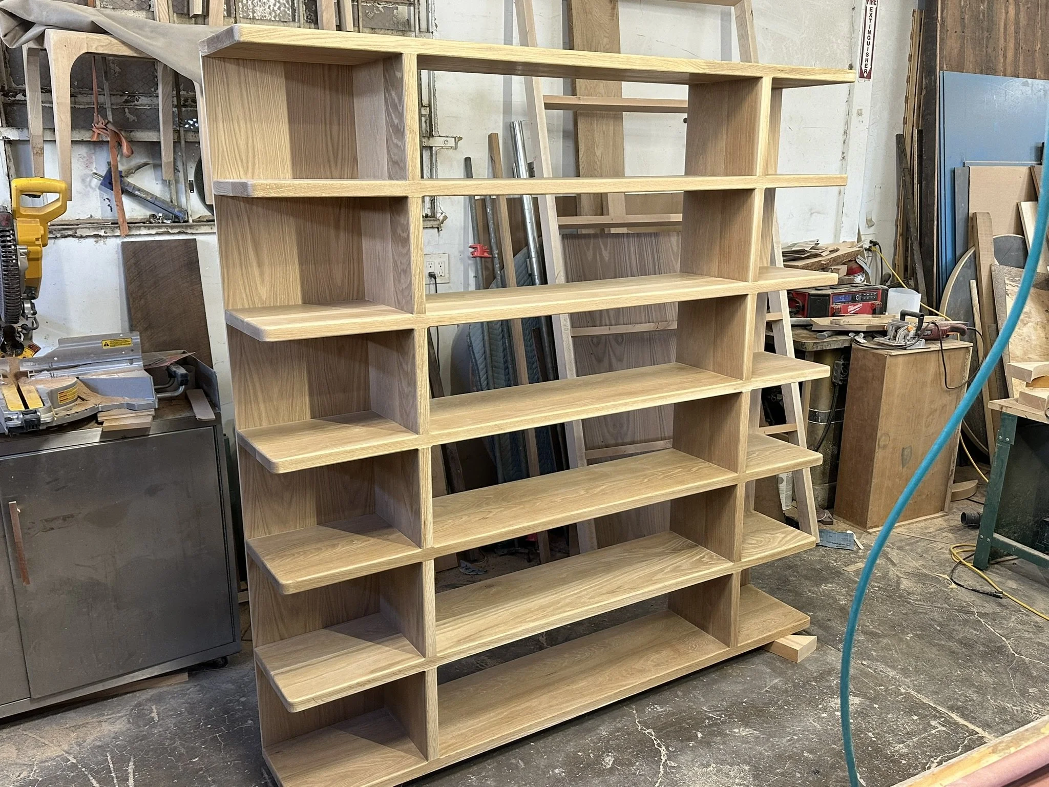 Wooden bookshelf with multiple open compartments in a workshop setting, surrounded by tools and materials.