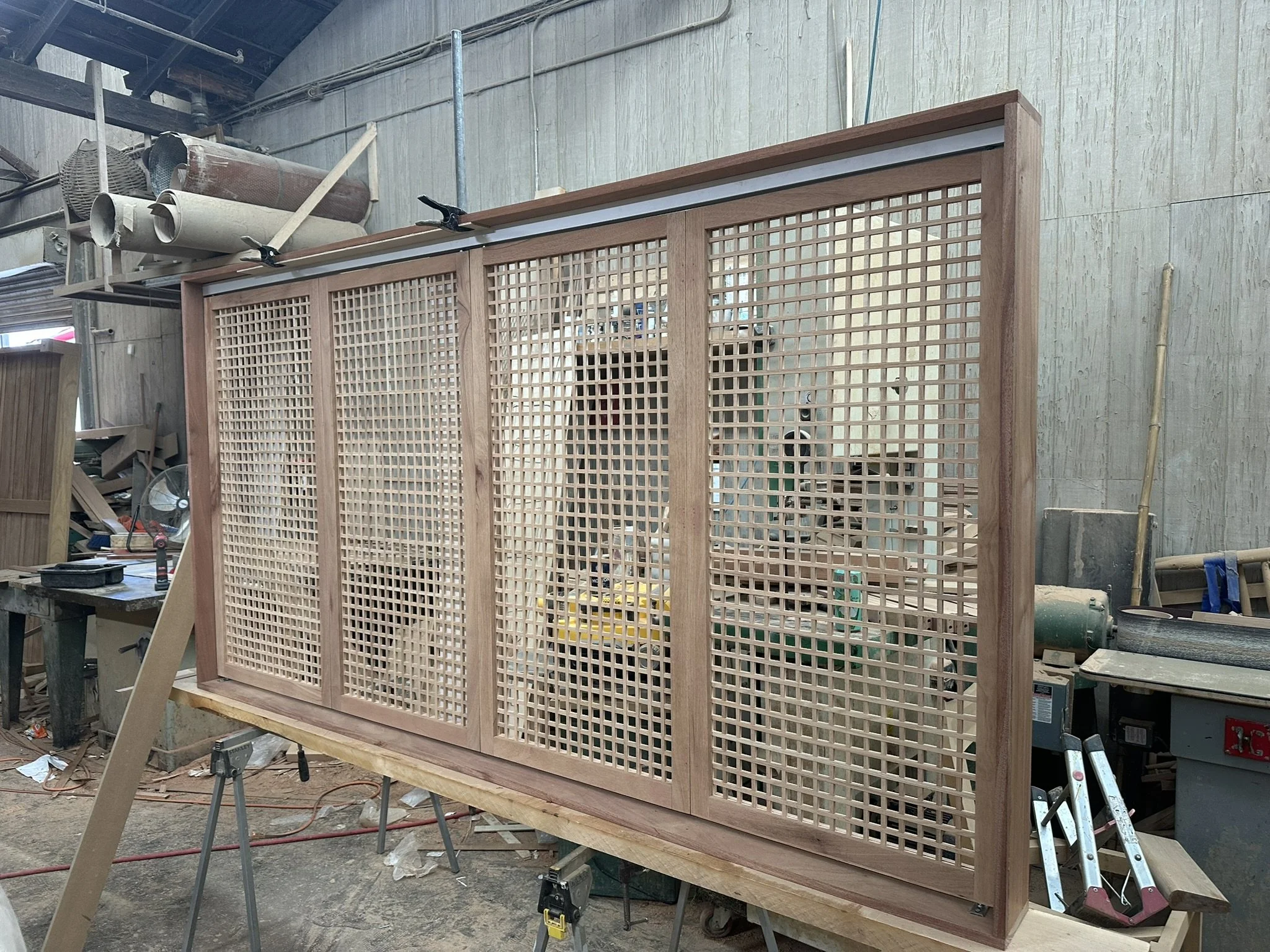 Wooden indoor or outdoor divider with a lattice design. Located in a workshop with various tools and materials in the background.