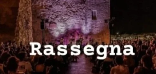 Un evento all'aperto con un pubblico seduto di fronte a una scena con luci colorate e la parola 'Rassegna' sovrapposta.