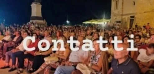 Pubblico seduto all'aperto con un'insegna luminosa che dice 'Contatti'.