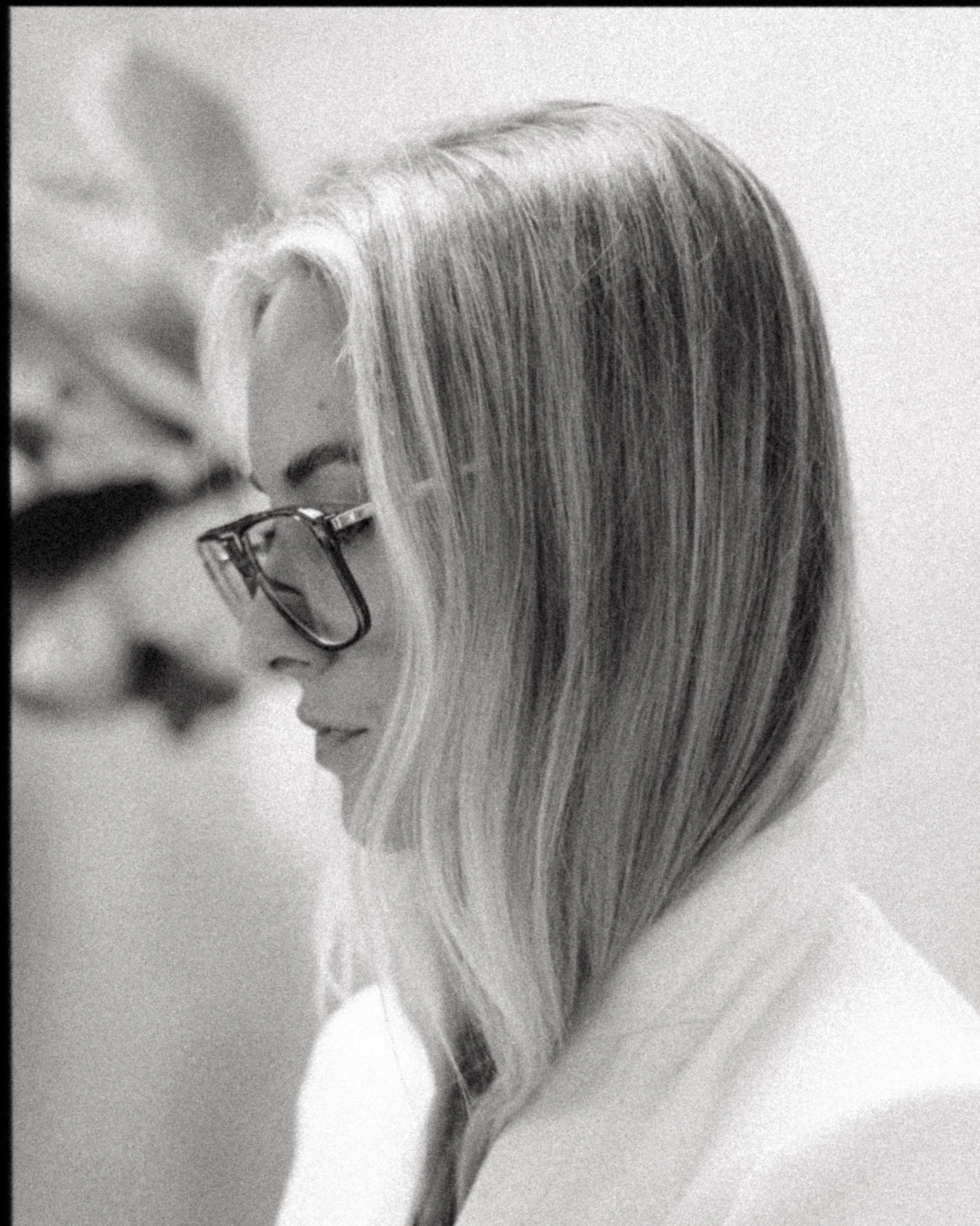 Close-up black and white photograph of a person with long hair wearing glasses, with their face in profile turned downward. Cam Carlson, Founder of BTS Collective Co.