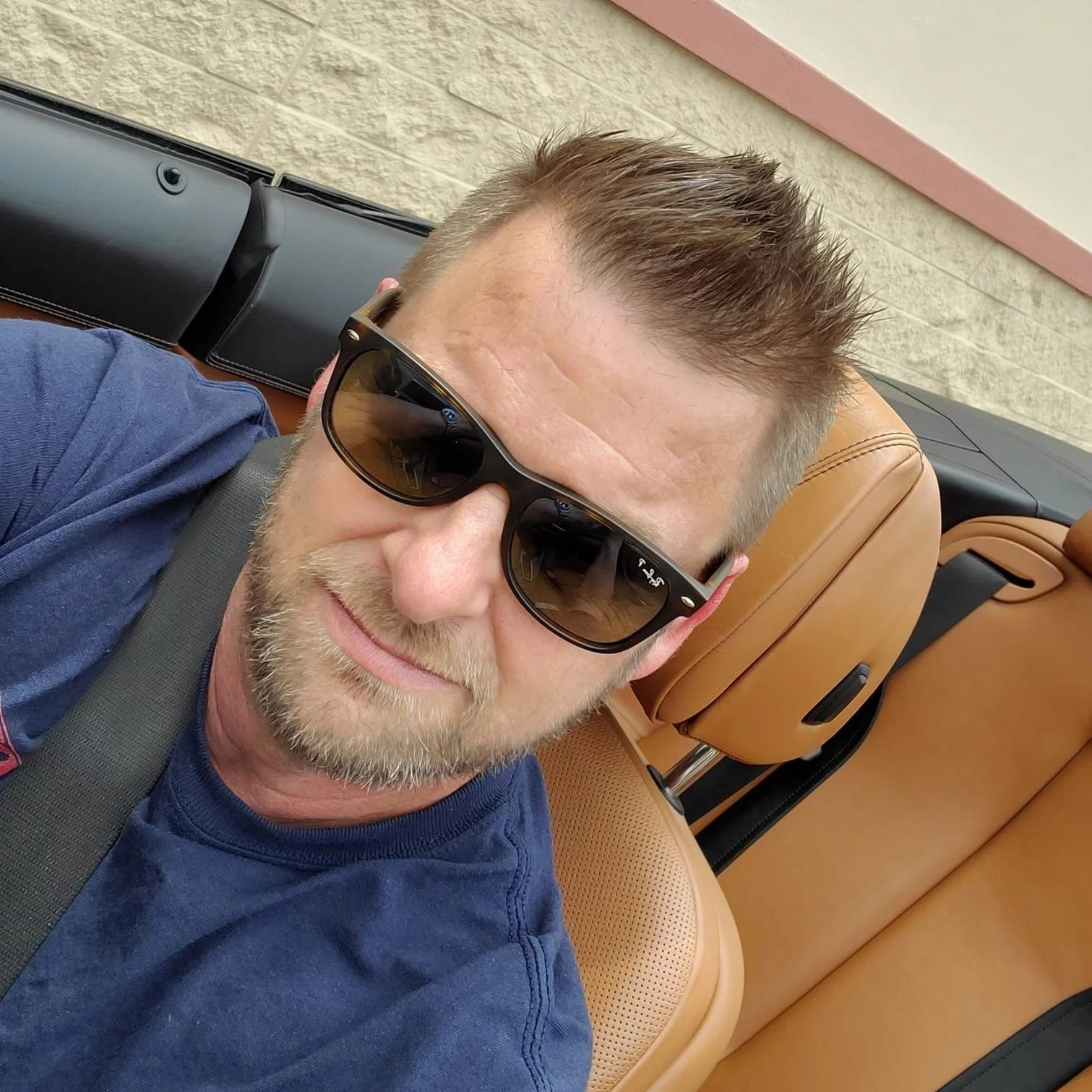 Portrait of Jeffrey Connell, a man with sunglasses and a beard, sitting in a car interior.