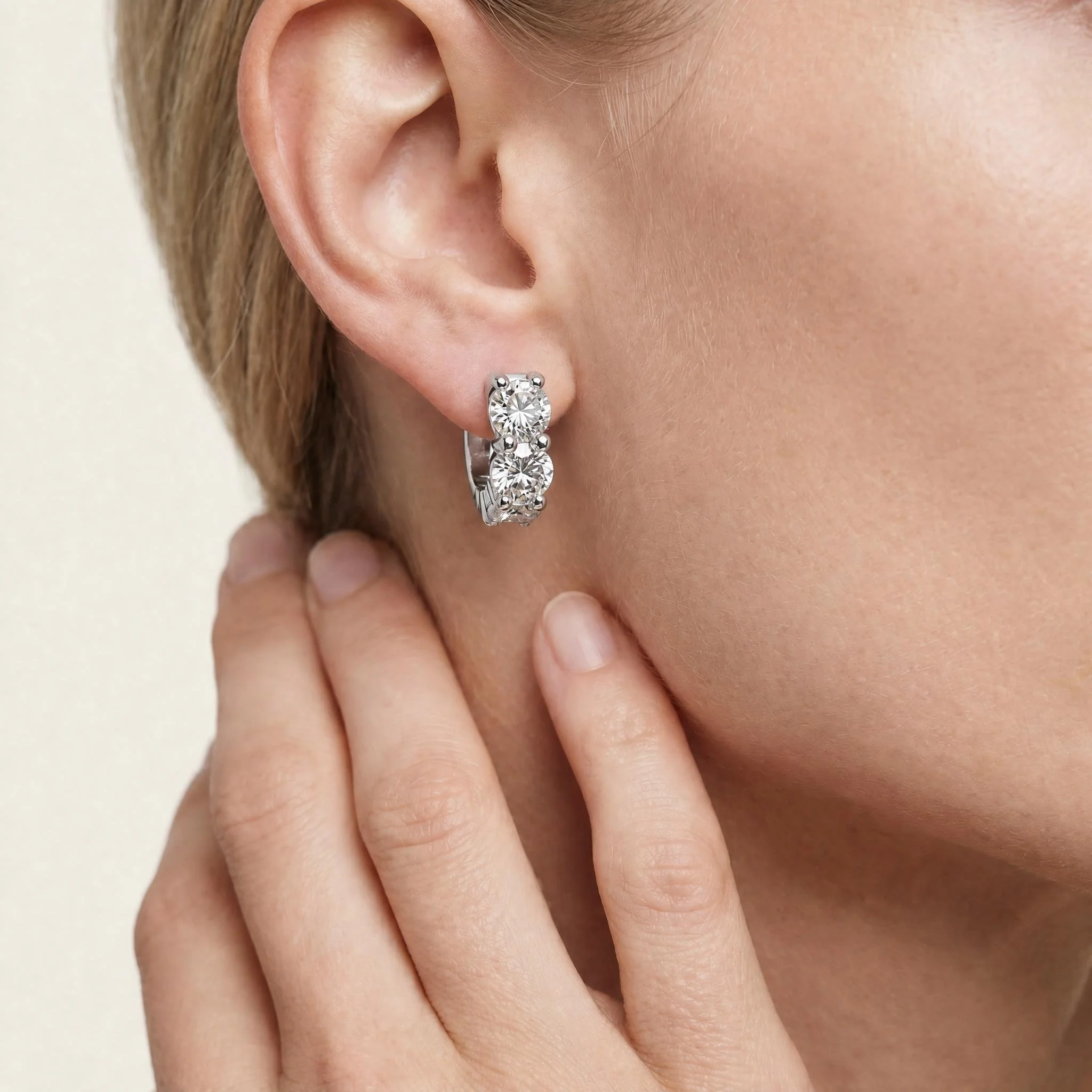 Close-up of a woman's ear, featuring a large diamond stud earring and her light skin with a few fine hair strands.