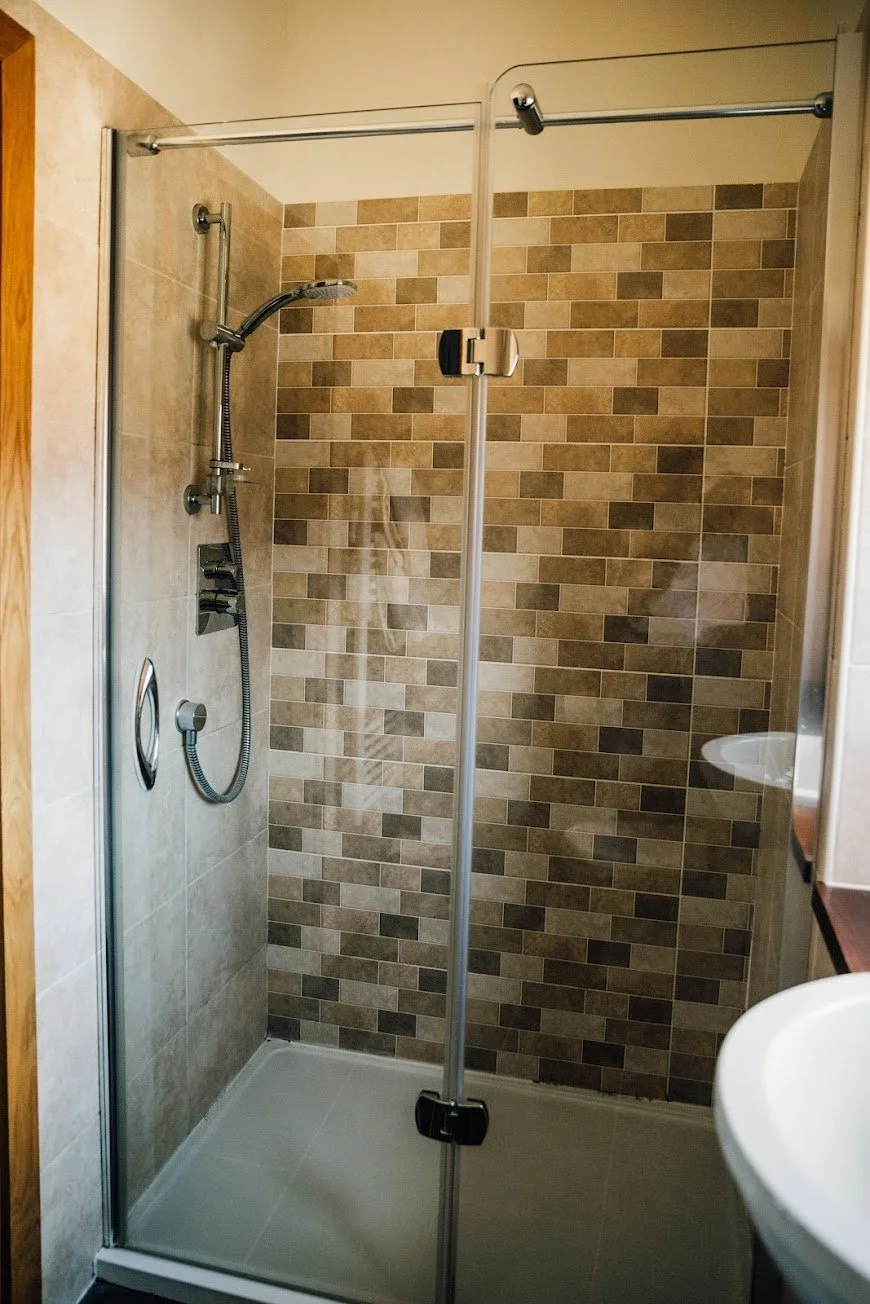 A walk-in shower with beige wall tiles, a handheld showerhead, and a glass door.