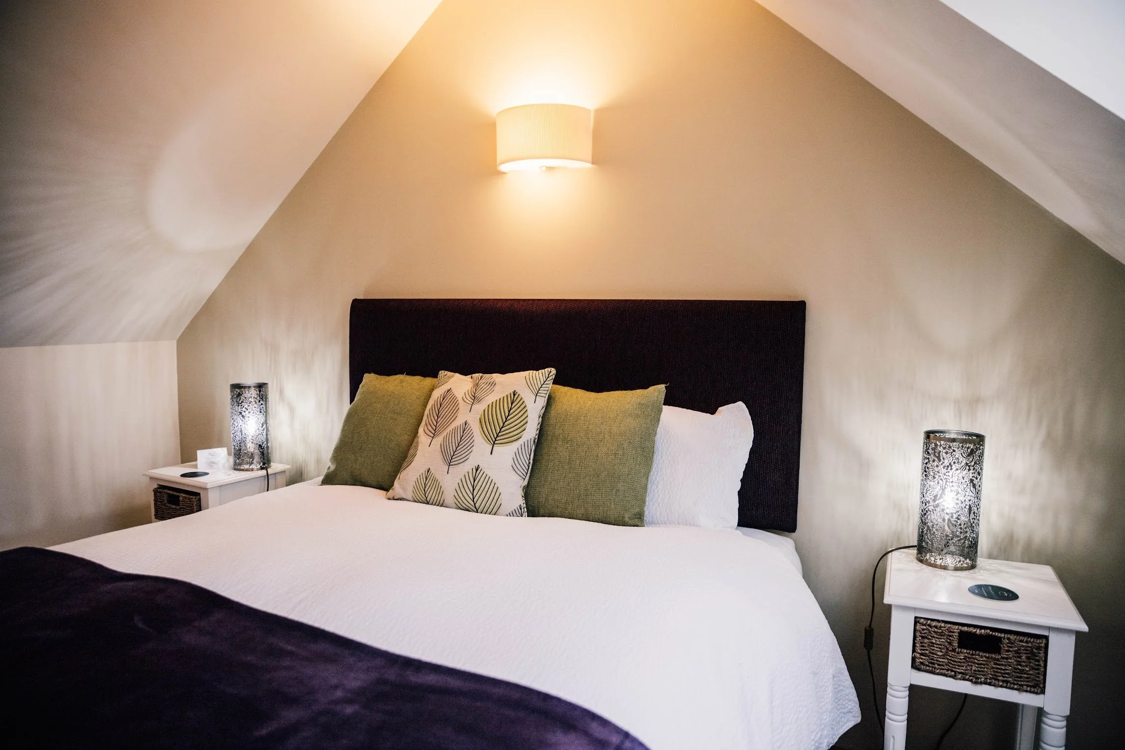 A bedroom with a bed, nightstands, and lamps on each side, featuring a black headboard and decorative pillows.