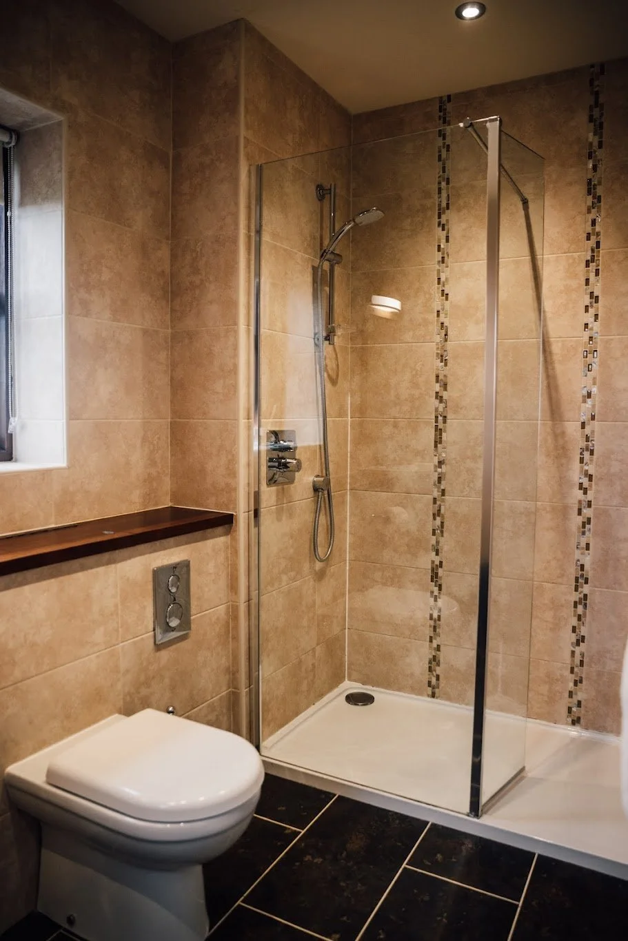 A modern bathroom with a walk-in shower featuring tan tiles, a glass shower partition, and a white toilet.