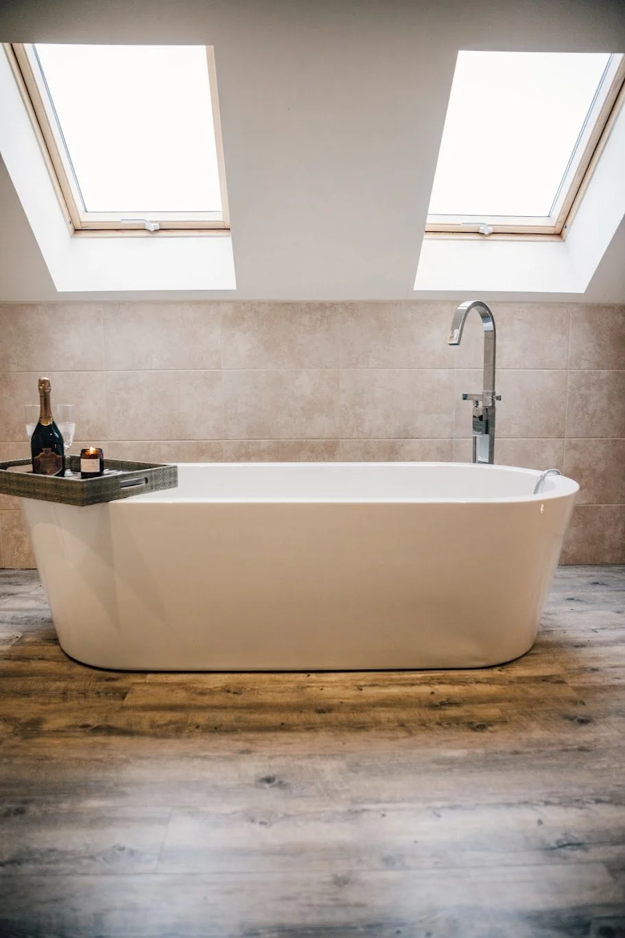 A modern bathroom with a white freestanding bathtub, two skylight windows above, and a wooden floor.