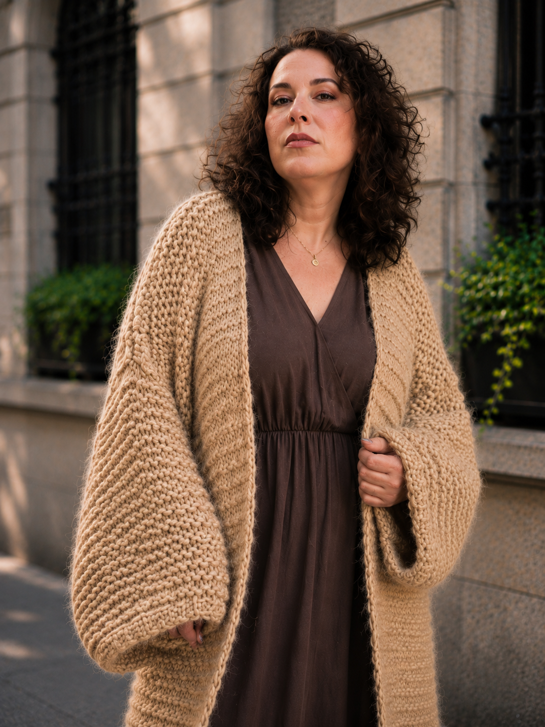beige chunky cardigan worked in garter stitch, worn by curly hair middle aged woman, chic and elegant look, designer outfit, bulky cardigan worn over coffee brown maxi dress and high heel boots