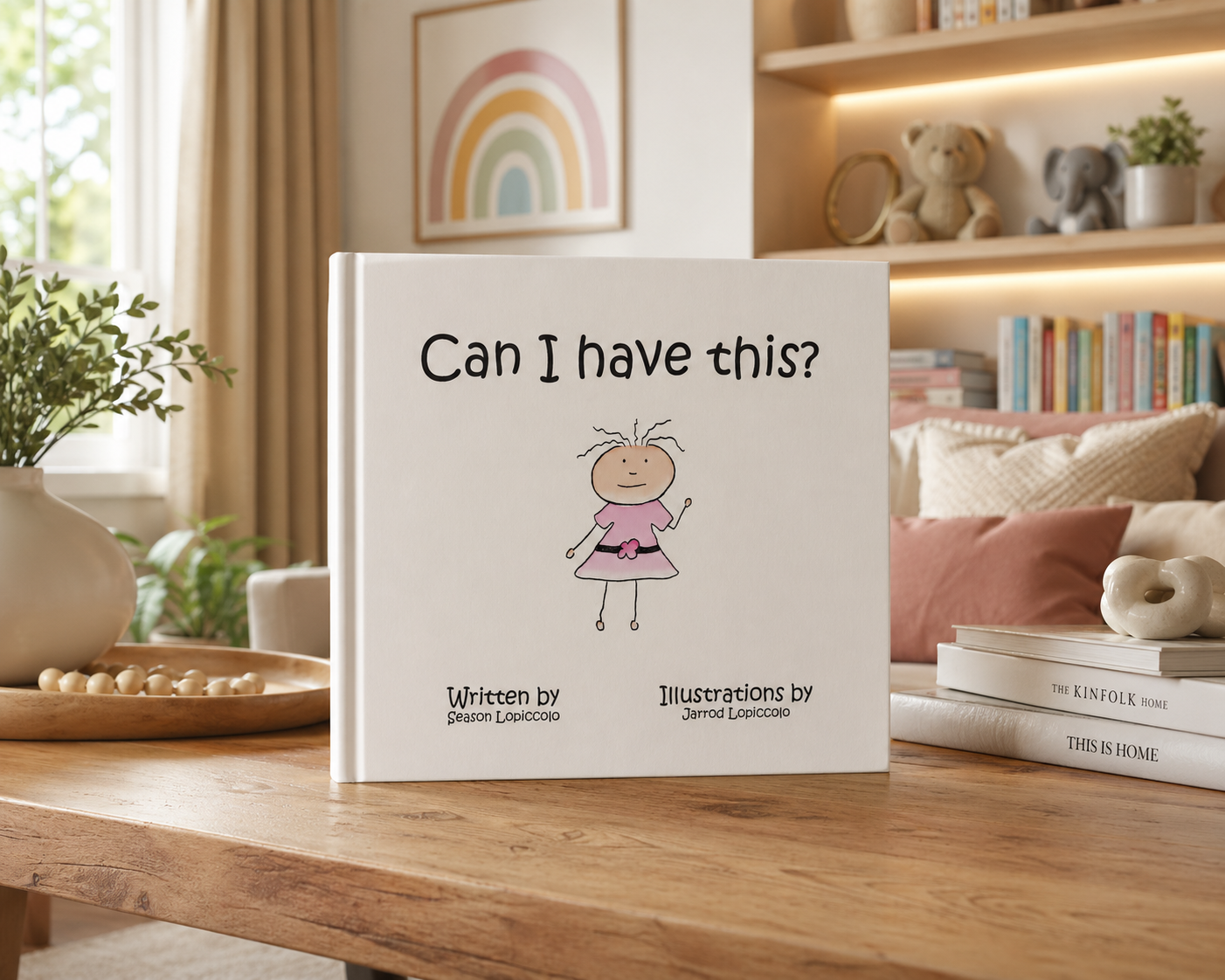 Children's book titled 'Can I have this?' with an illustrated girl on the cover, placed on a wooden table in a cozy living room with books and decorative items.