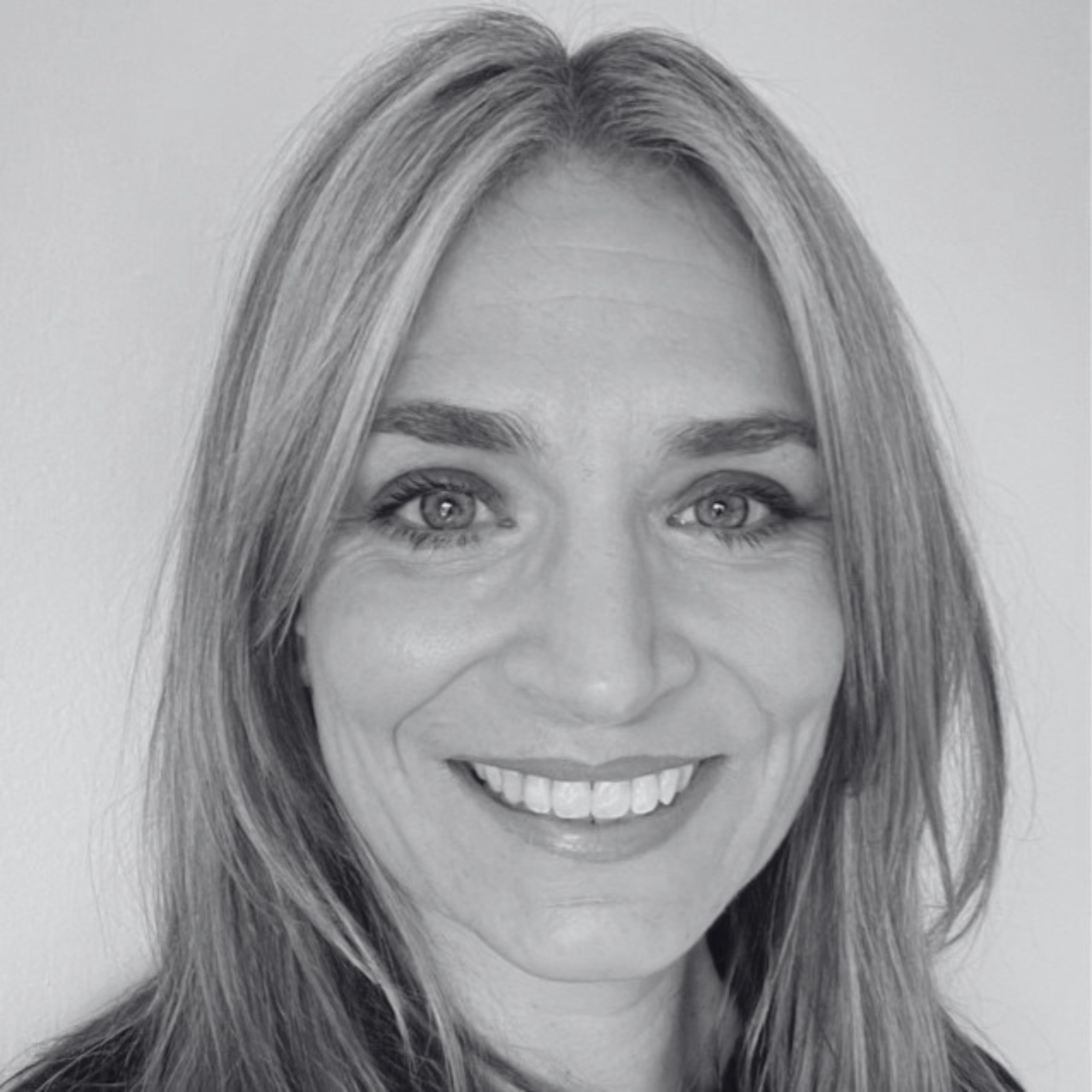 A black and white portrait photograph of a woman with light-colored hair, bright eyes, and a big smile showing her teeth.