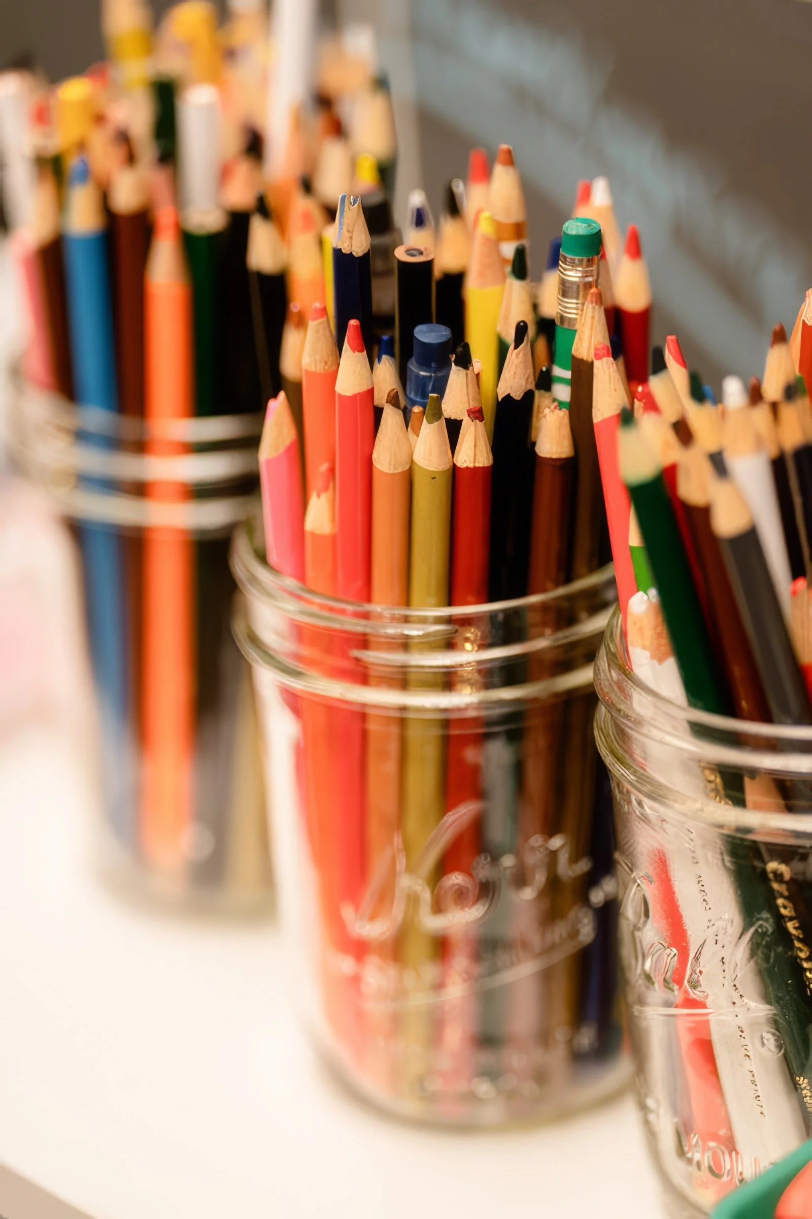 Close-up of colorful colored pencils held in a glass container with some writing tools in the background.