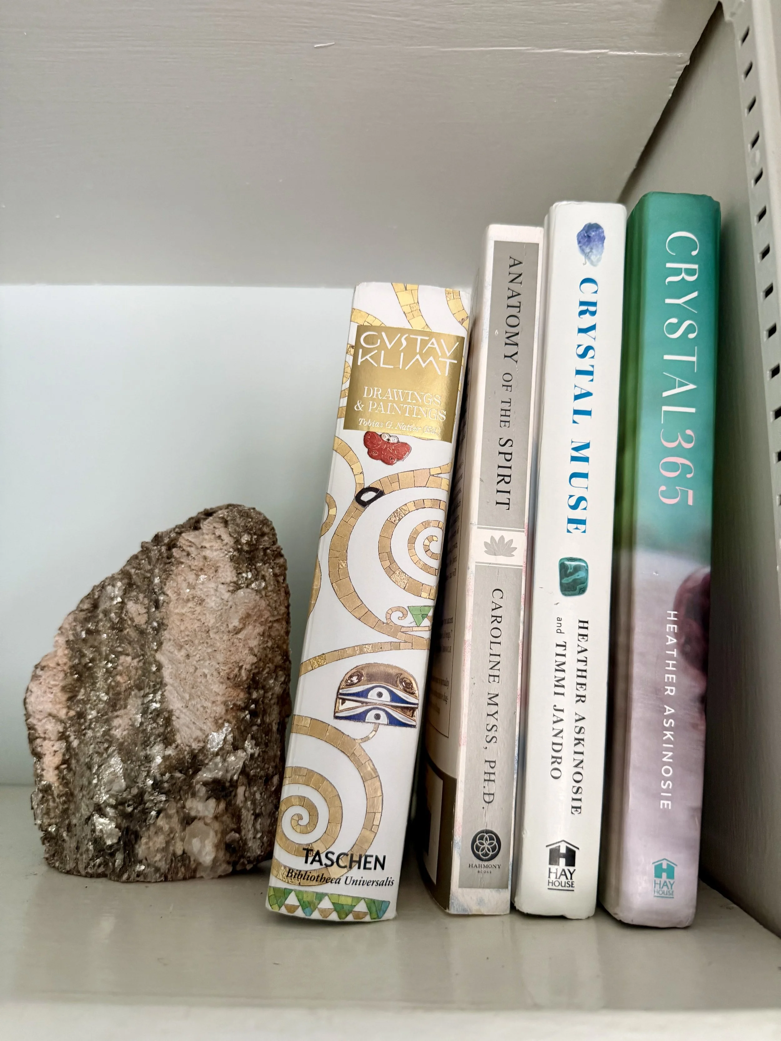 A large mineral or stone beside four books on a shelf.