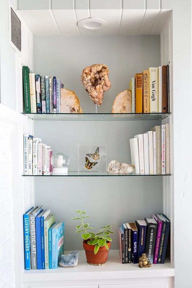 Decorative bookshelf with framed photographs, crystals, feathers, beads, and various books.