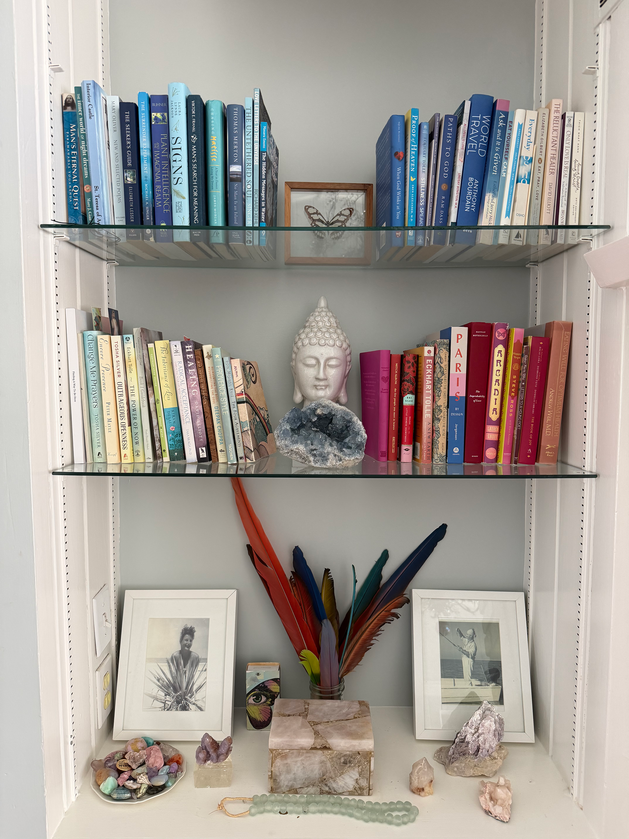Decorative bookshelf with framed photographs, crystals, feathers, beads, and various books.