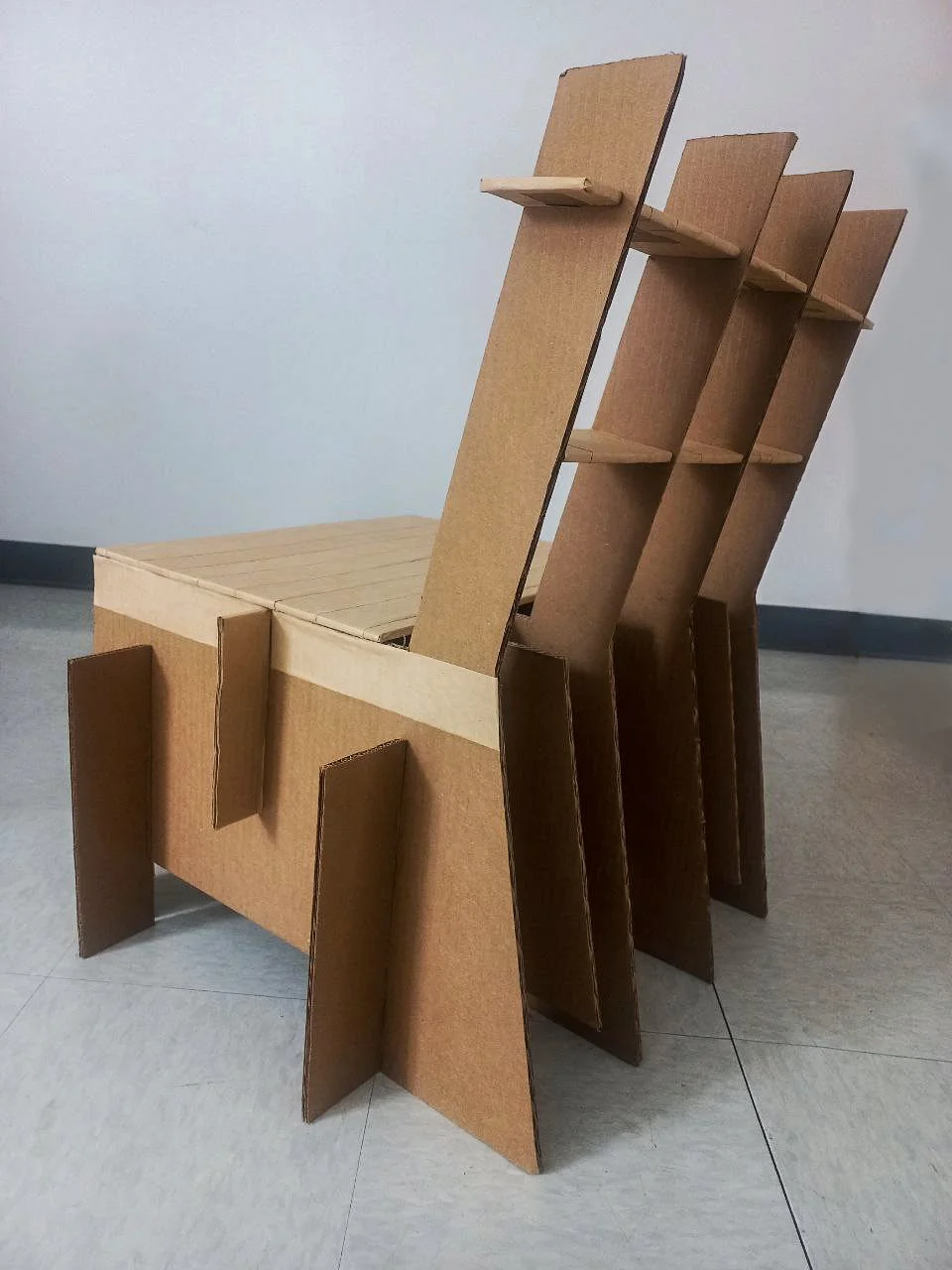 A cardboard chair with a flat seat, four legs, and three attached ladder-back slats with shelves.