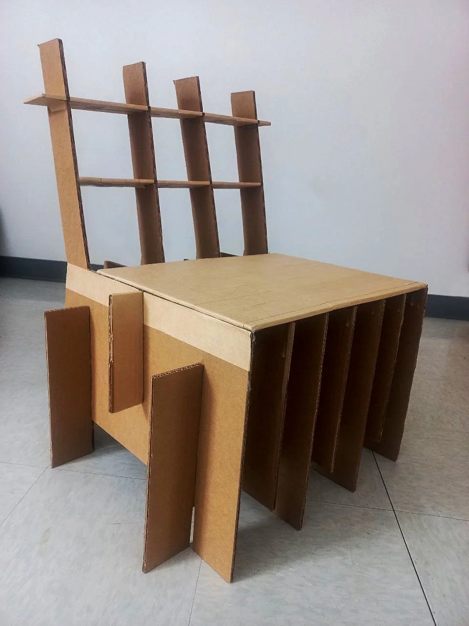 A chair constructed from cardboard with a backrest and armrests, featuring a grid-like design with multiple vertical and horizontal panels.
