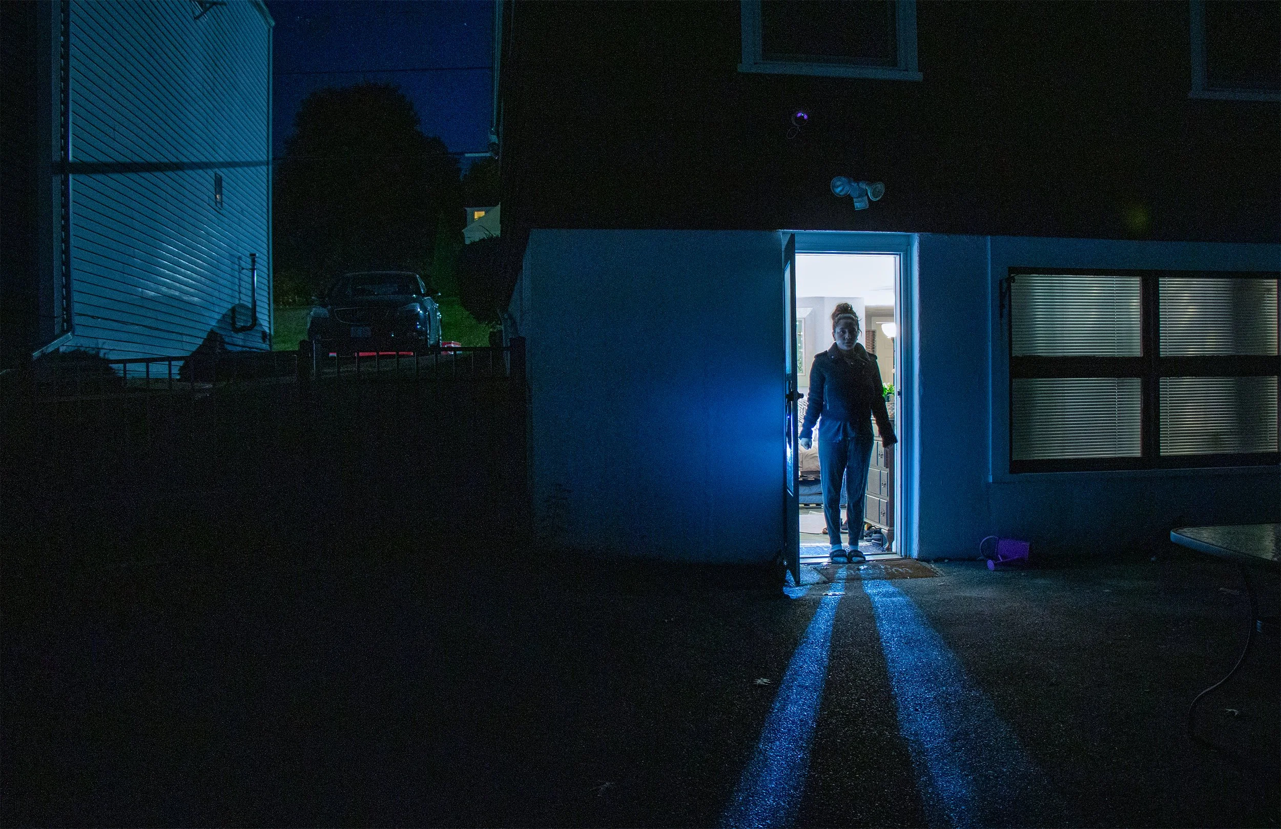 A woman standing in an open doorway of a building at night, with light illuminating her and the ground outside.