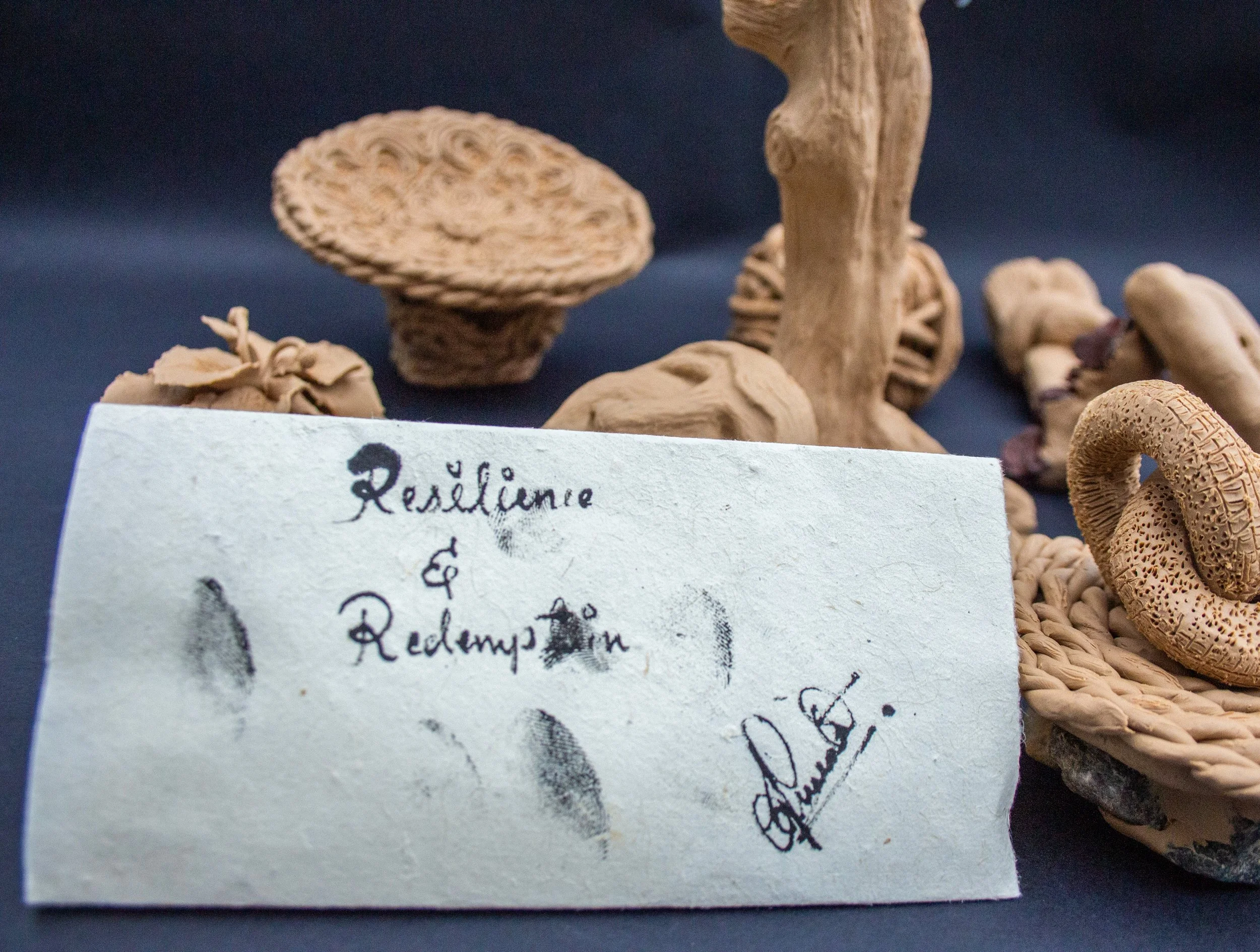 Various dried mushrooms on a dark surface with a handwritten note in front that reads 'Resilience & Redamping' with fingerprints and a signature.