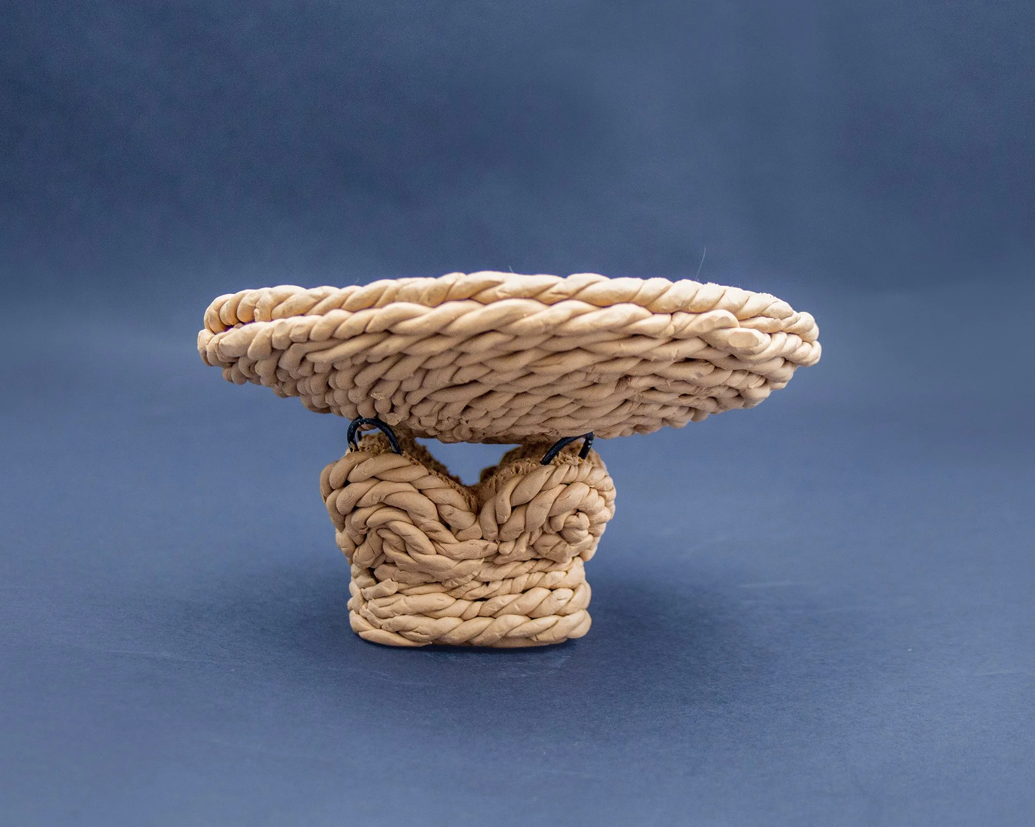 A small decorative sculpture resembling a toilet crafted from intertwined beige-colored rope against a blue background.