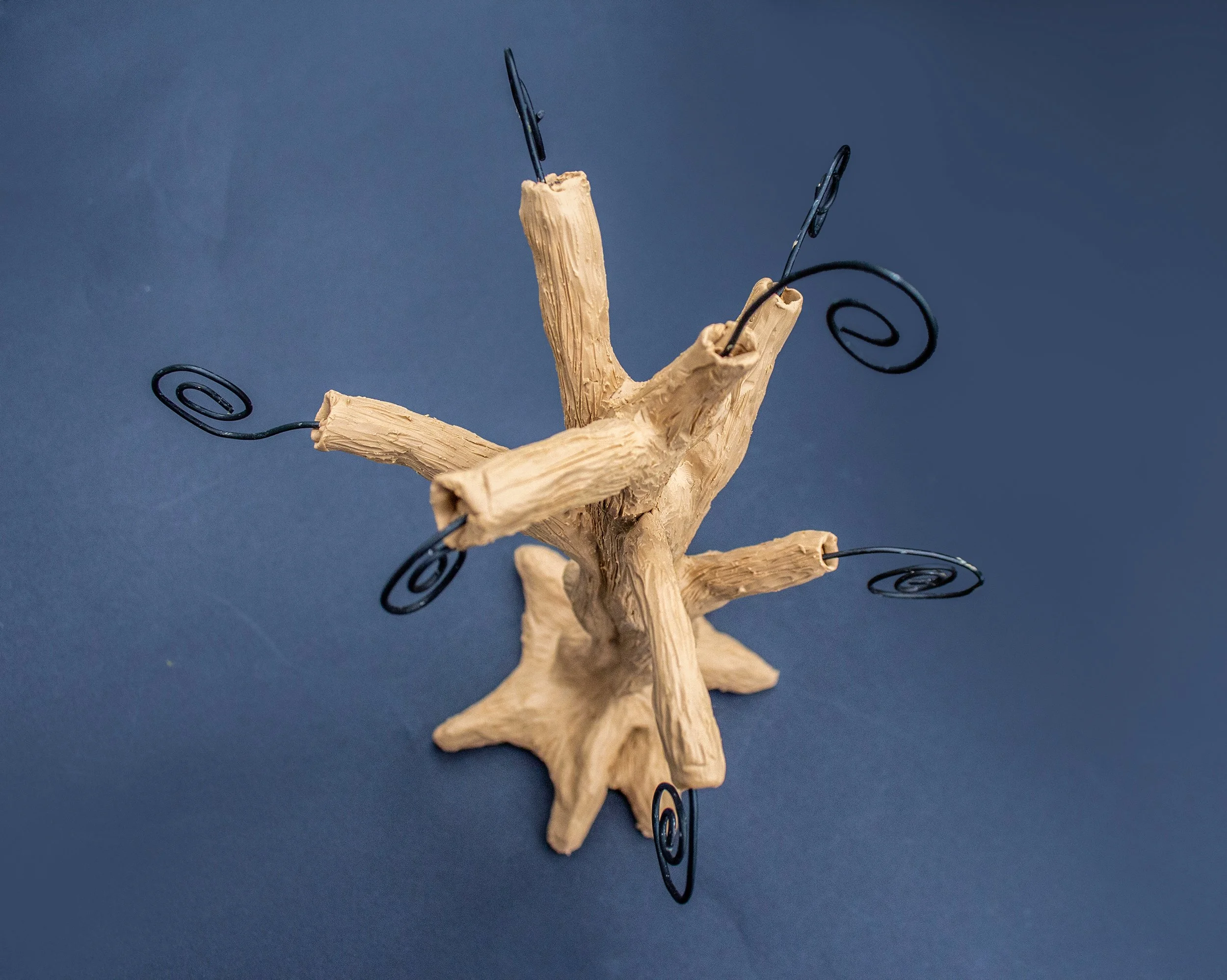 A decorative tabletop piece resembling a miniature tree with a central wooden branch structure and black wire spirals extending from the tips, set against a blue background.