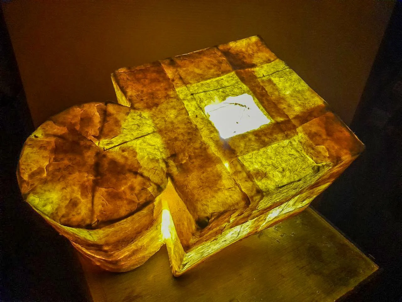Illuminated decorative paper lantern with a layered design in warm yellow and orange tones placed on a wooden surface.
