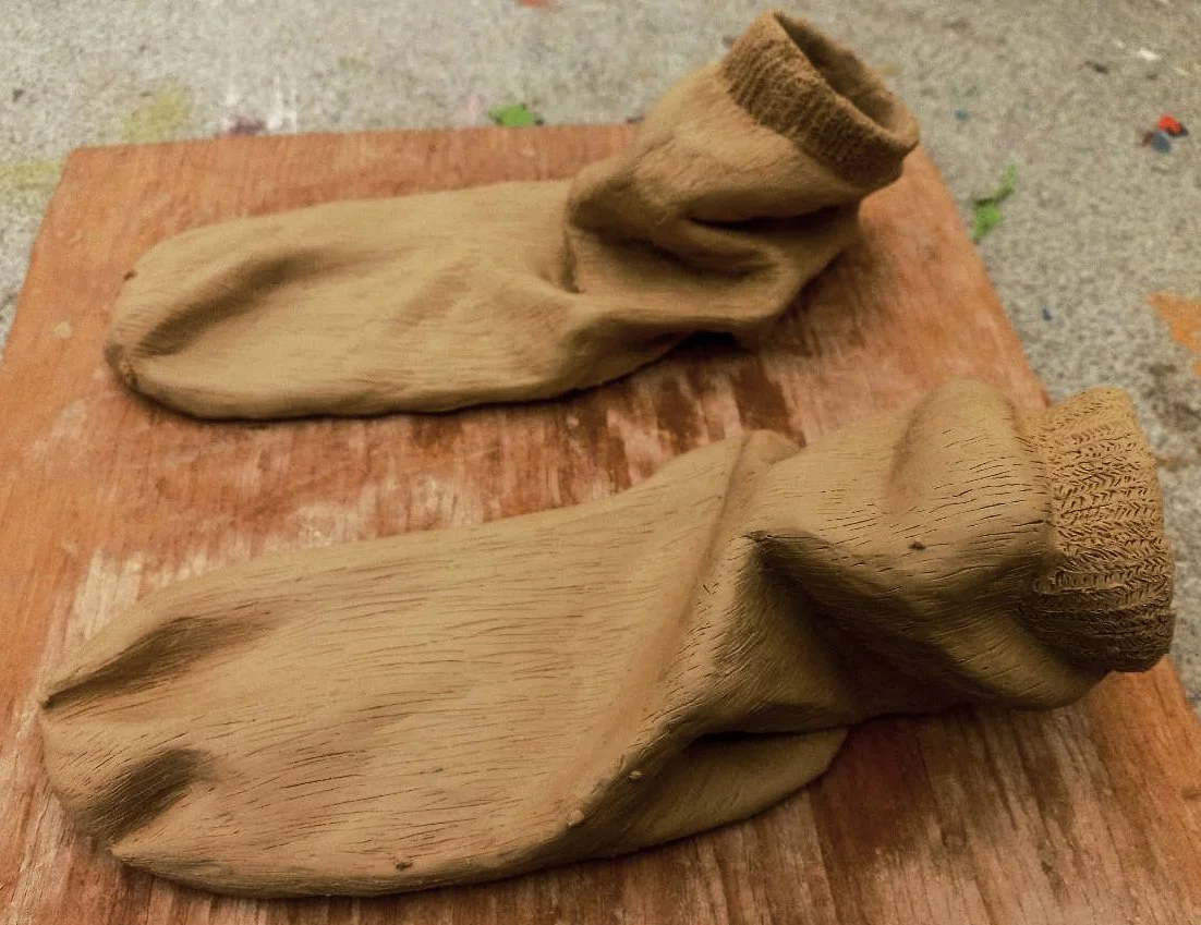 Two carved wooden sculptures resembling slippers or shoes on a wooden surface.