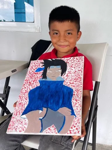 A young boy holding a colorful painted portrait of a woman with dark hair, glasses, and a blue jacket, in a classroom setting.