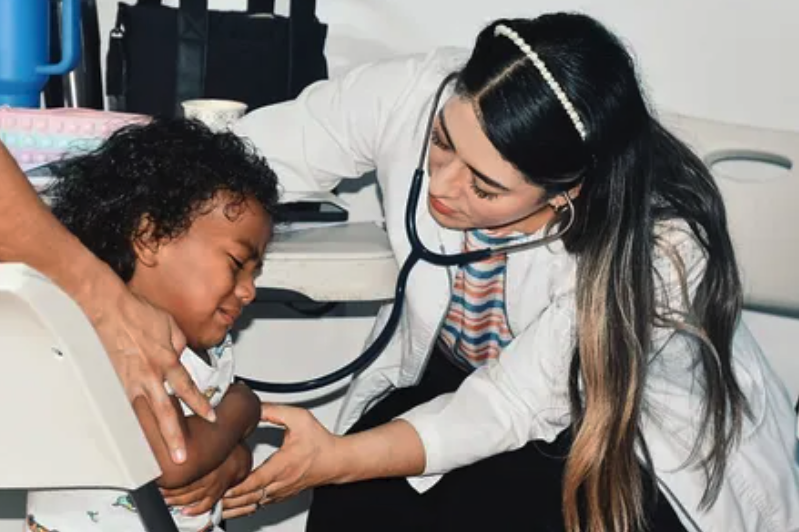 A young girl with curly hair receiving a check-up from a female doctor in a hospital setting.