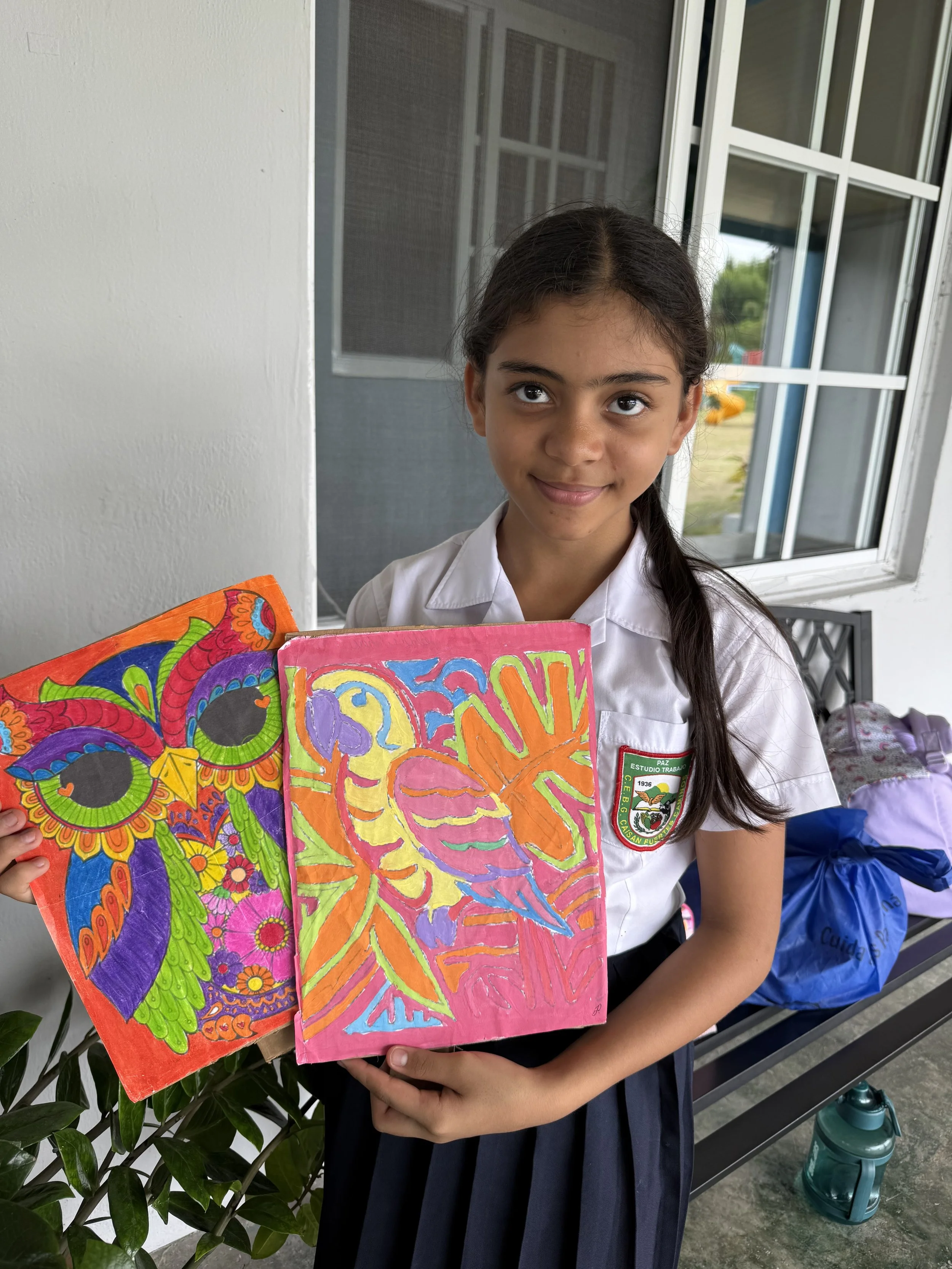A young girl in a school uniform holding colorful artwork during daytime.