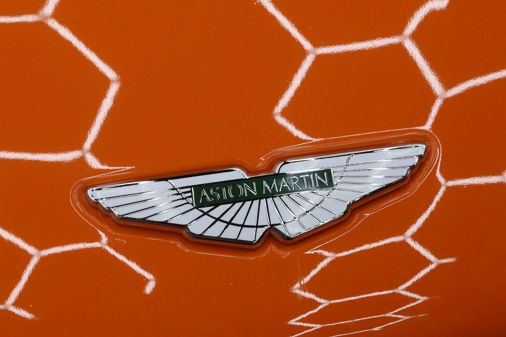 Close-up of an Aston Martin logo on an orange car with a white honeycomb pattern