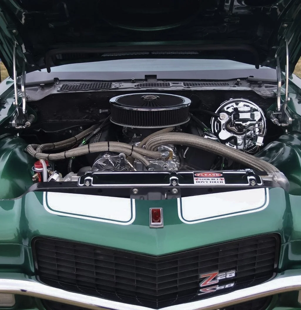 The hood of a green Chevrolet Z28 Camaro with the engine exposed, showing a chrome air filter, various hoses, and engine components.
