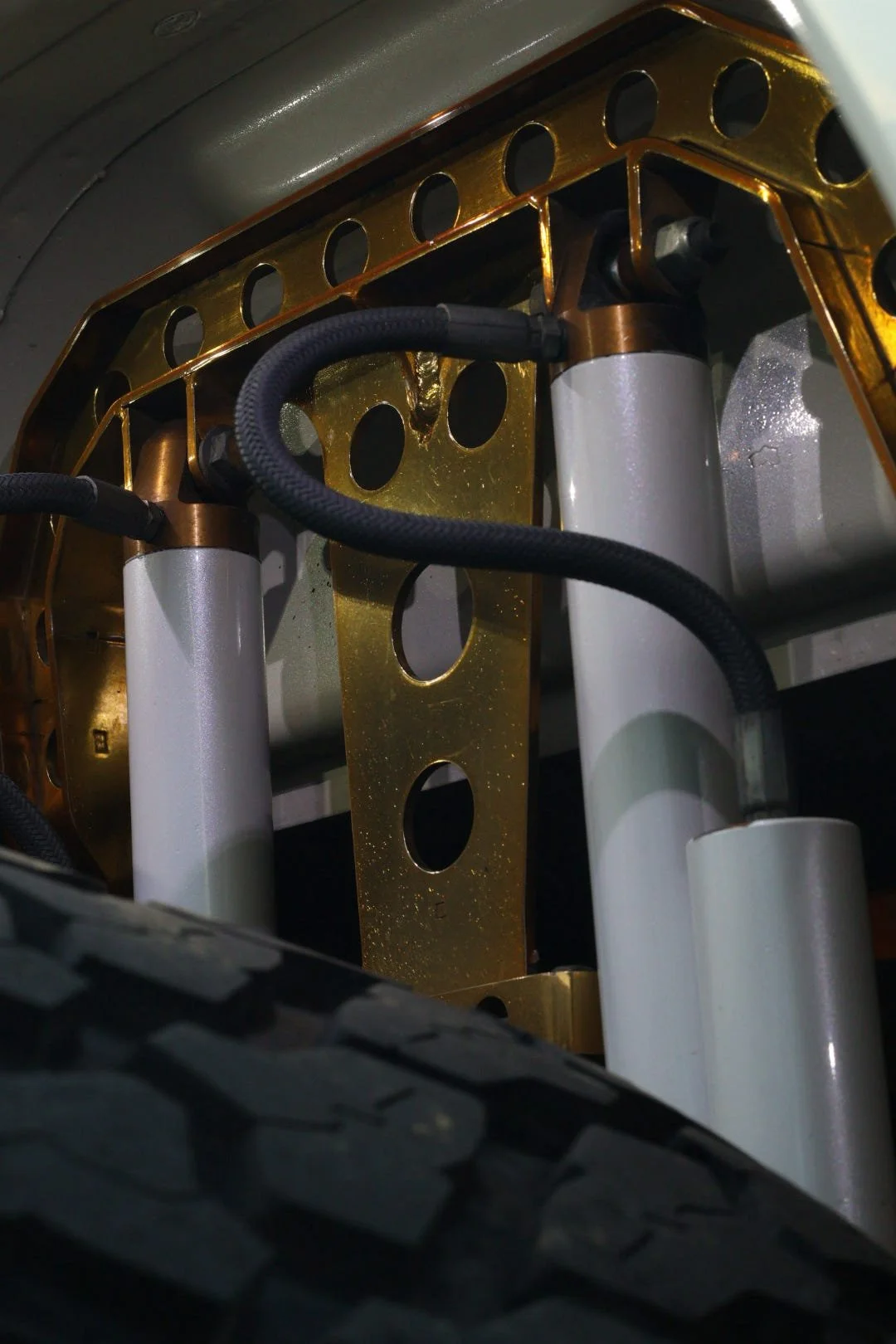 Close-up view of the suspension system inside a vehicle, showing suspension struts, a gold-colored support bracket, and a tire tread in the foreground.