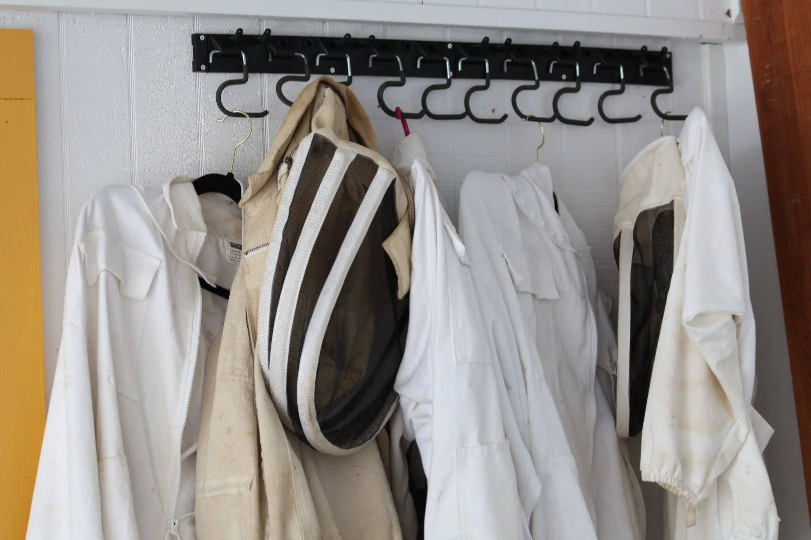 White fencing jackets hanging on hooks, with some dirt and stains, on a wall-mounted coat rack with black hooks.