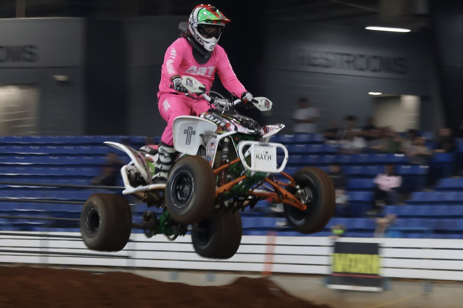 A person wearing a pink racing suit and helmet riding an ATV in an indoor arena.