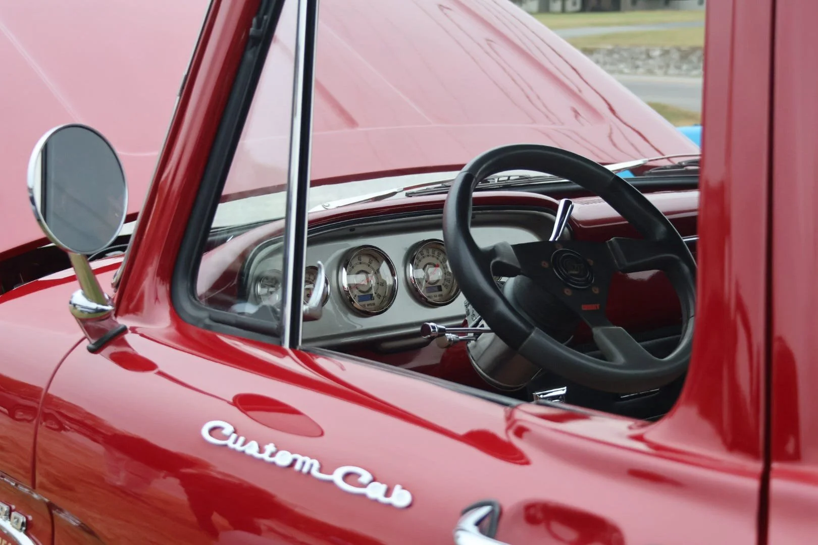Close-up of the interior of a vintage red Volkswagen Beetle, showing the dashboard, steering wheel, side mirror, and the words 'Custom Car' on the side.