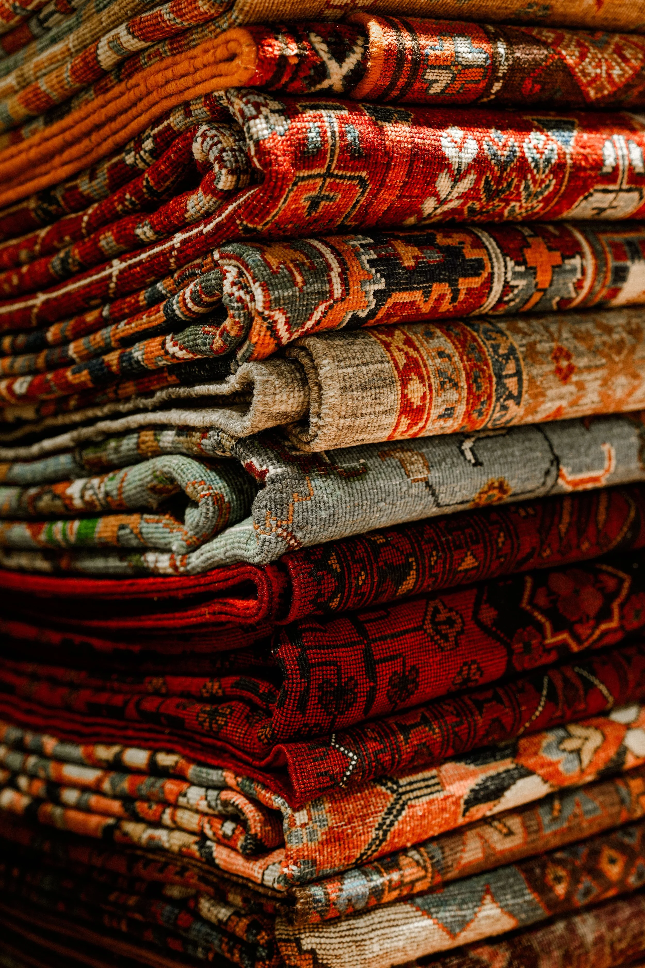 Stack of rolled oriental rugs with intricate patterns and vivid colors including red, orange, beige, and dark green.