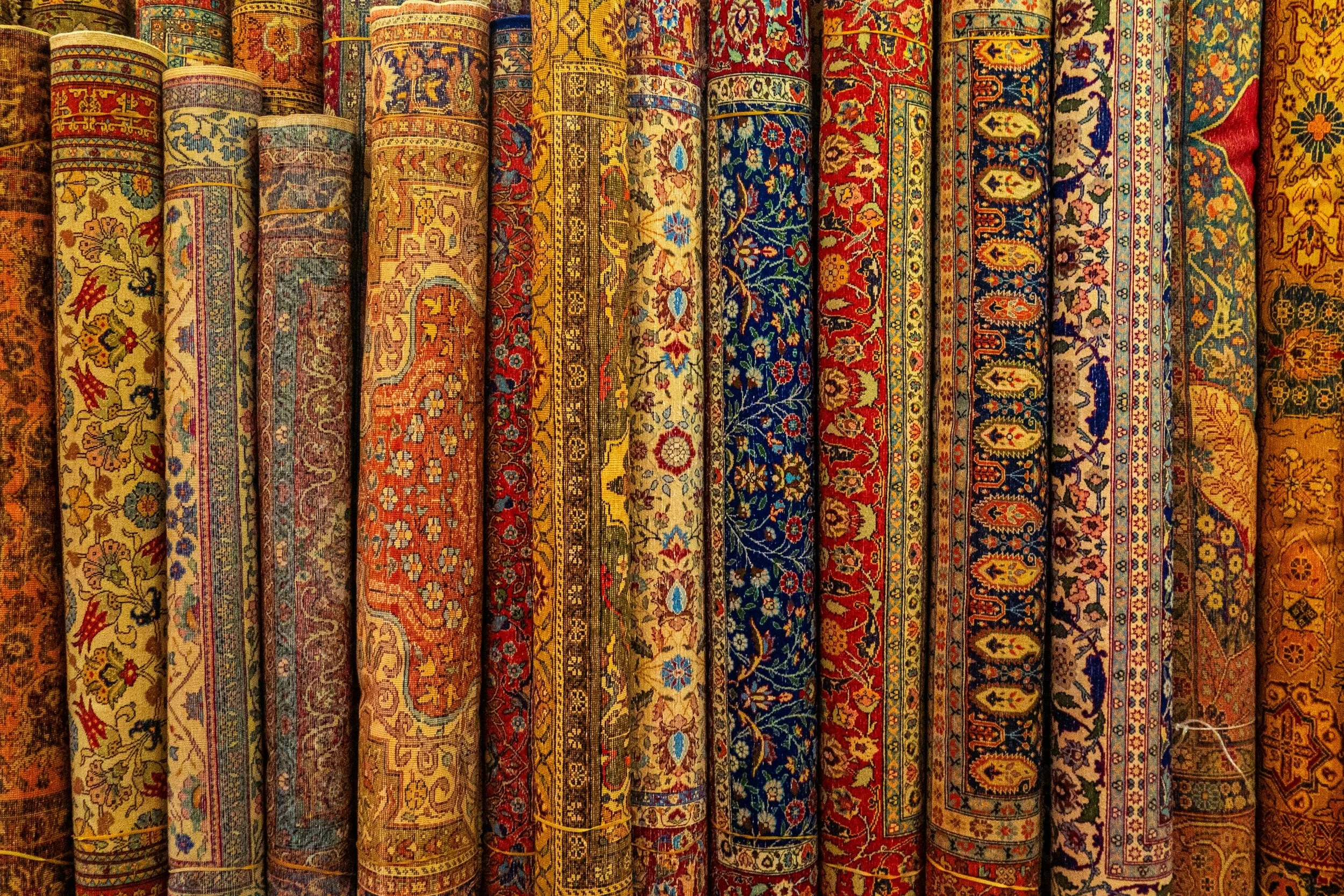 A row of rolled-up, colorful traditional Persian rugs with intricate floral and geometric patterns