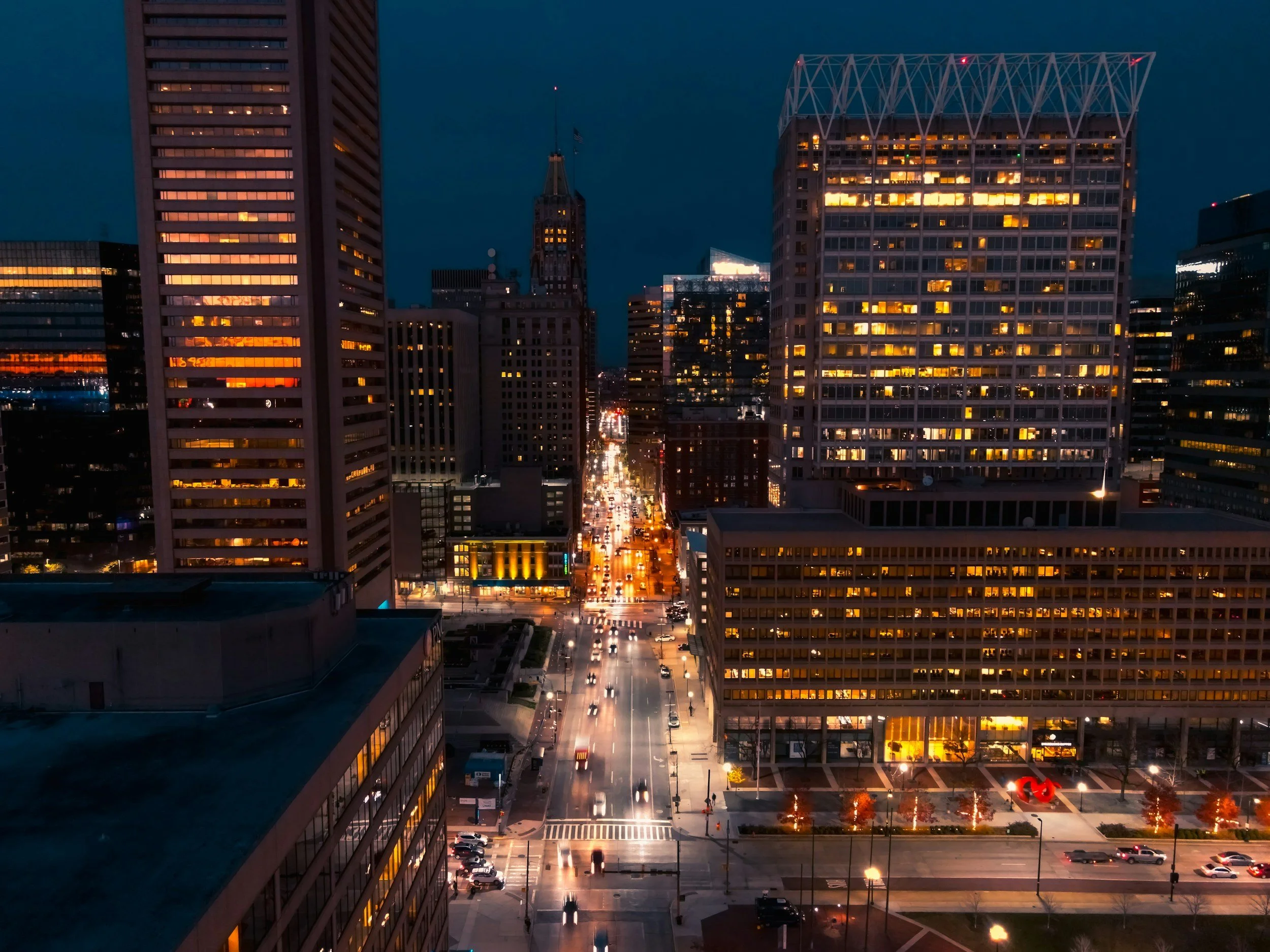 Cityscape at night with illuminated high-rise buildings, busy streets, and traffic lights.