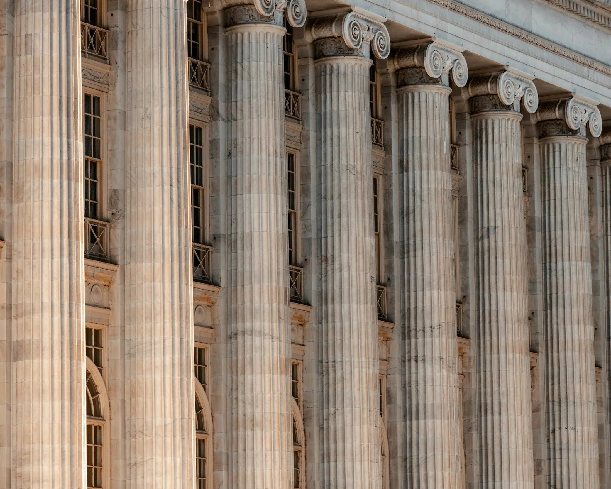 Close-up view of the exterior of a classical building with large marble columns featuring scrolls at the top and multiple windows with decorative framing.