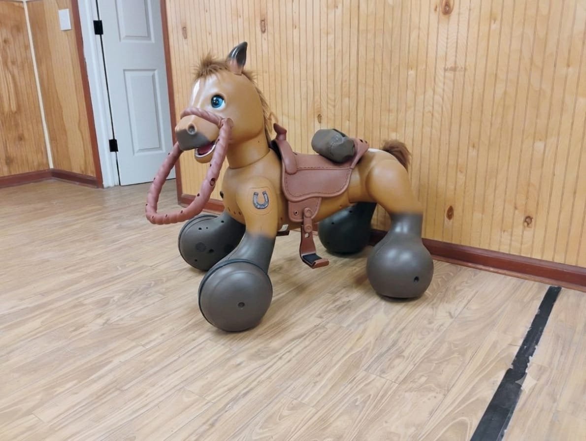 A plastic, toy horse with a saddle, bridle, and harness, designed for children to ride and play.