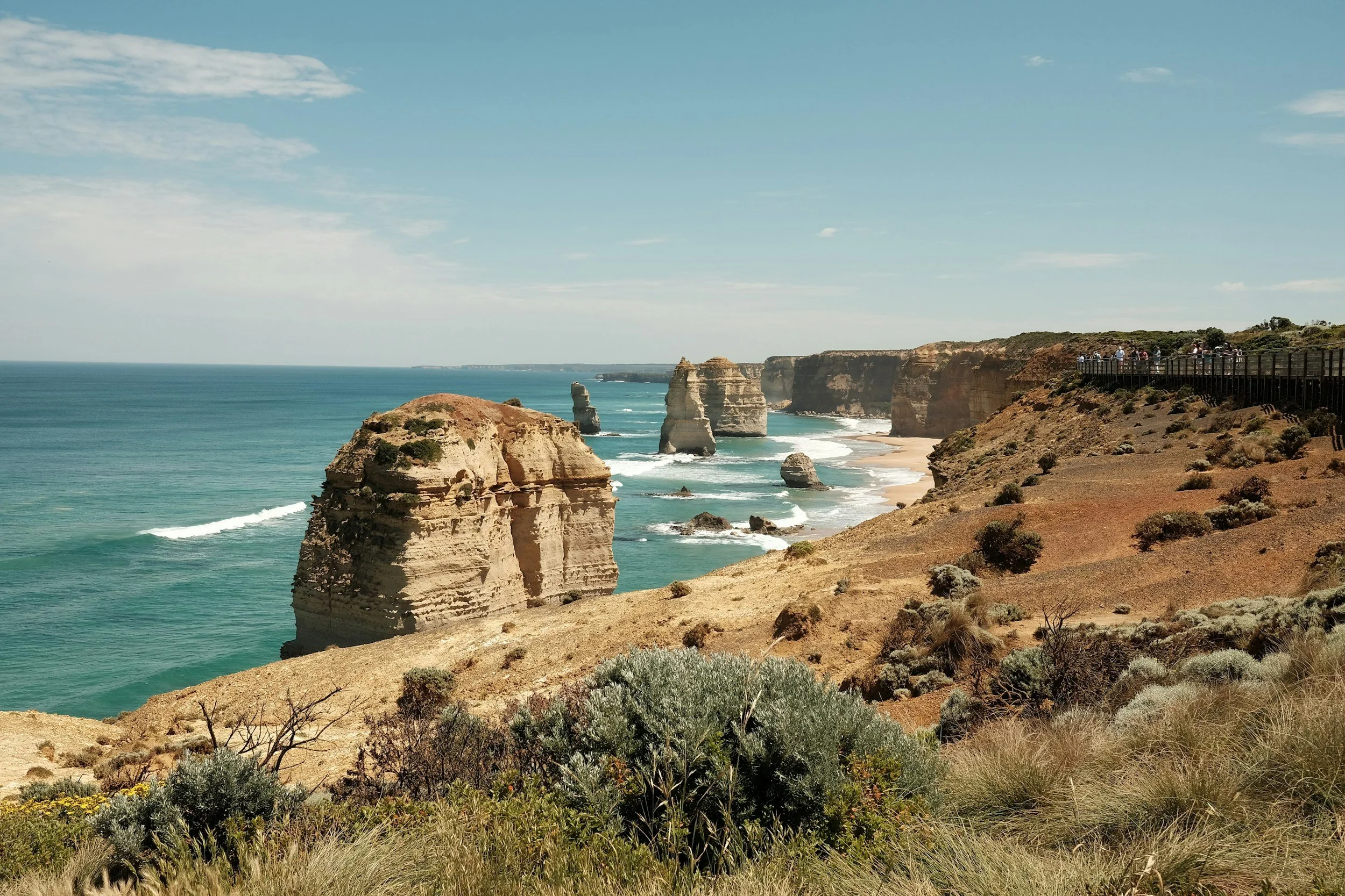 Coastal cliffs and rock formations along the ocean with a viewing platform and people observing the scenery.